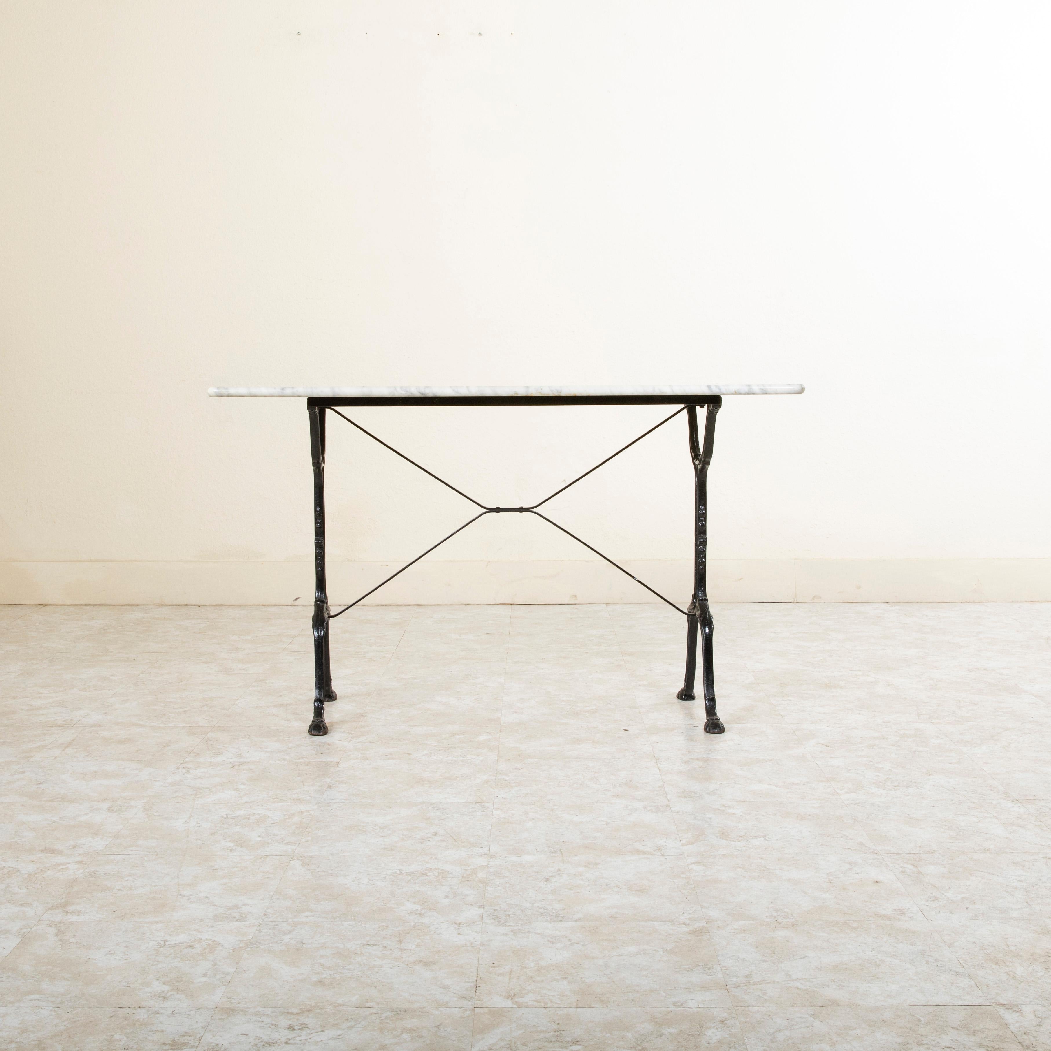 Originally used in a French brasserie during the early twentieth century, this long cast iron bistro table or cafe table features a solid white marble top with grey veining. Scrolled iron legs support the top and are joined by an X-stretcher that