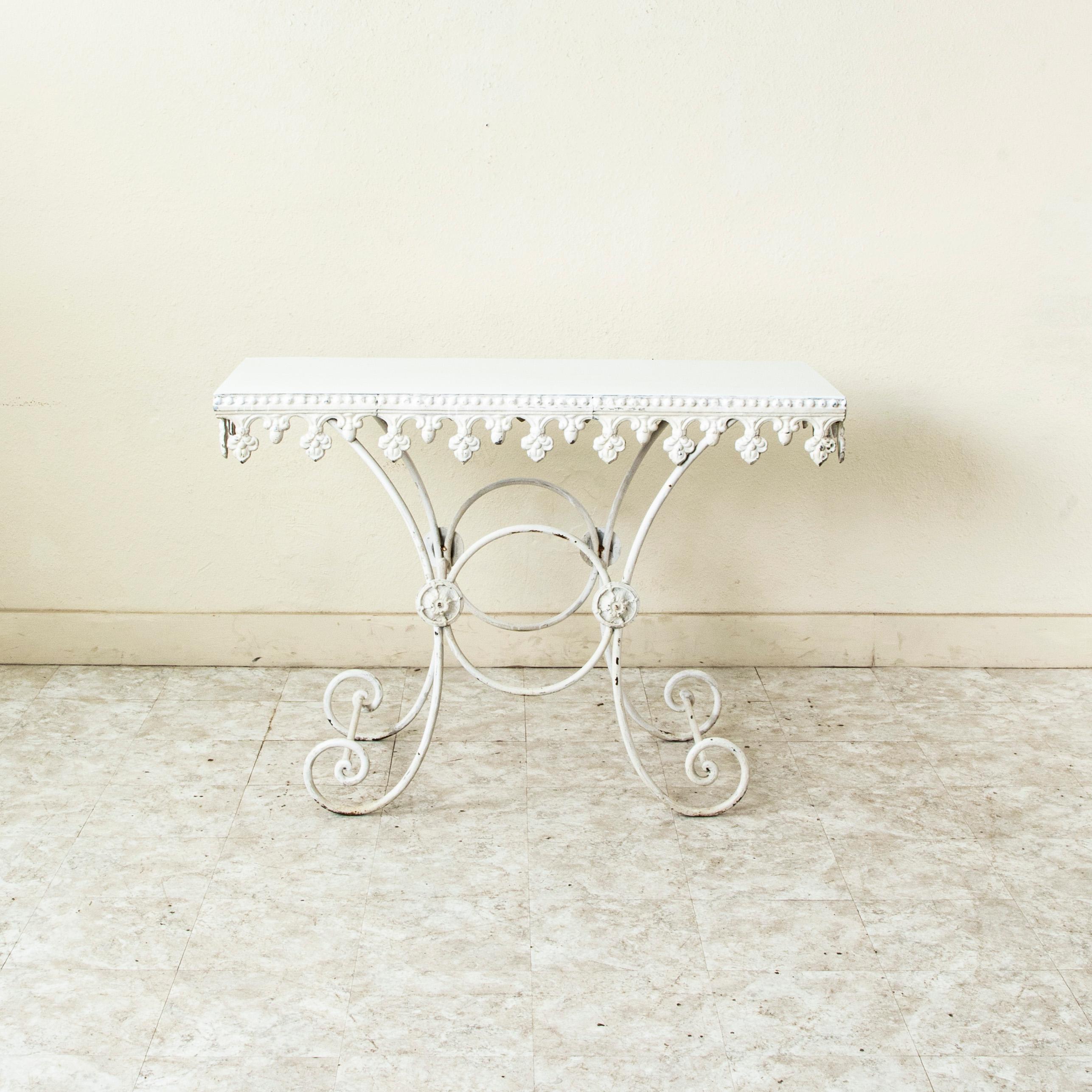 Esta mesa pastelera francesa de hierro fundido de principios del siglo XX tiene la parte superior de metal pintado de blanco. El delantal de debajo de la parte superior tiene detalles de pedrería y un dibujo de flor de lis. La parte superior