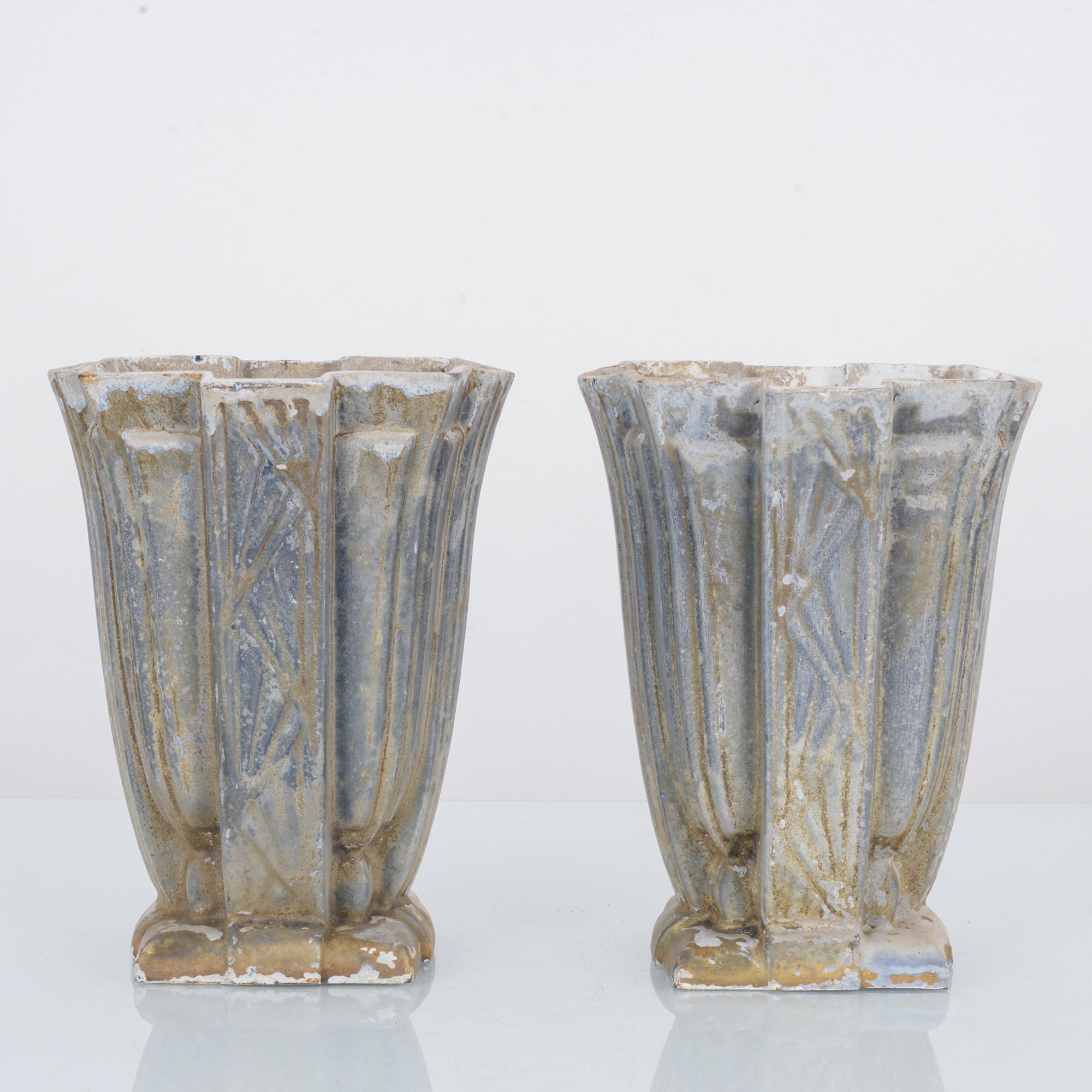 A pair of patinated cast iron planters hailing from France, circa 1900. With their proto-Art Deco design, they look like inspiration for the Chrysler building,-while their own design is naturally inspired in the wild daffodil.