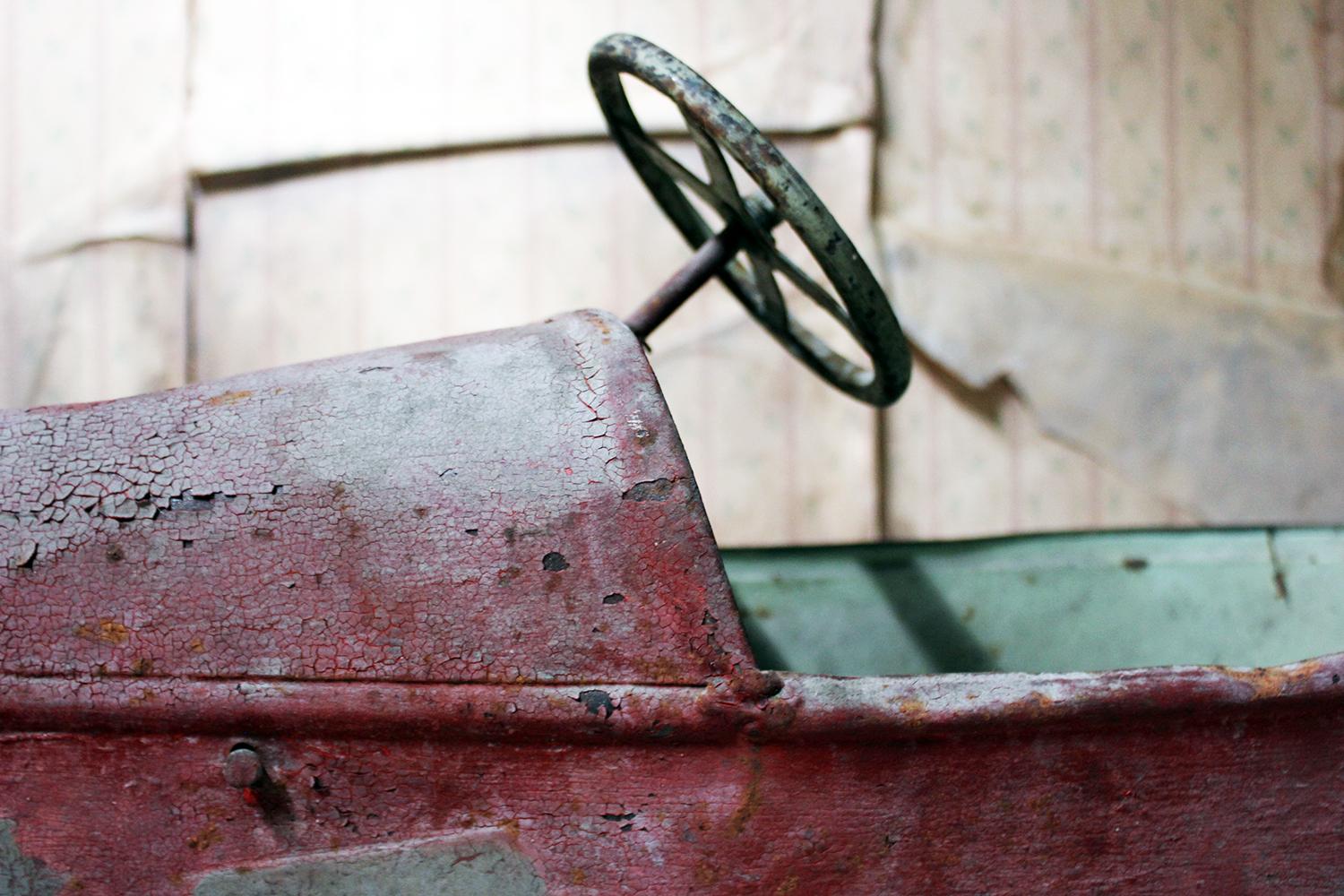 In beautifully untouched condition, the child’s pedal racing car, having a wonderfully worn ruby red painted surface, with a pea green interior and steering wheel, accompanied by an original period photograph of the former owner with her cat, the