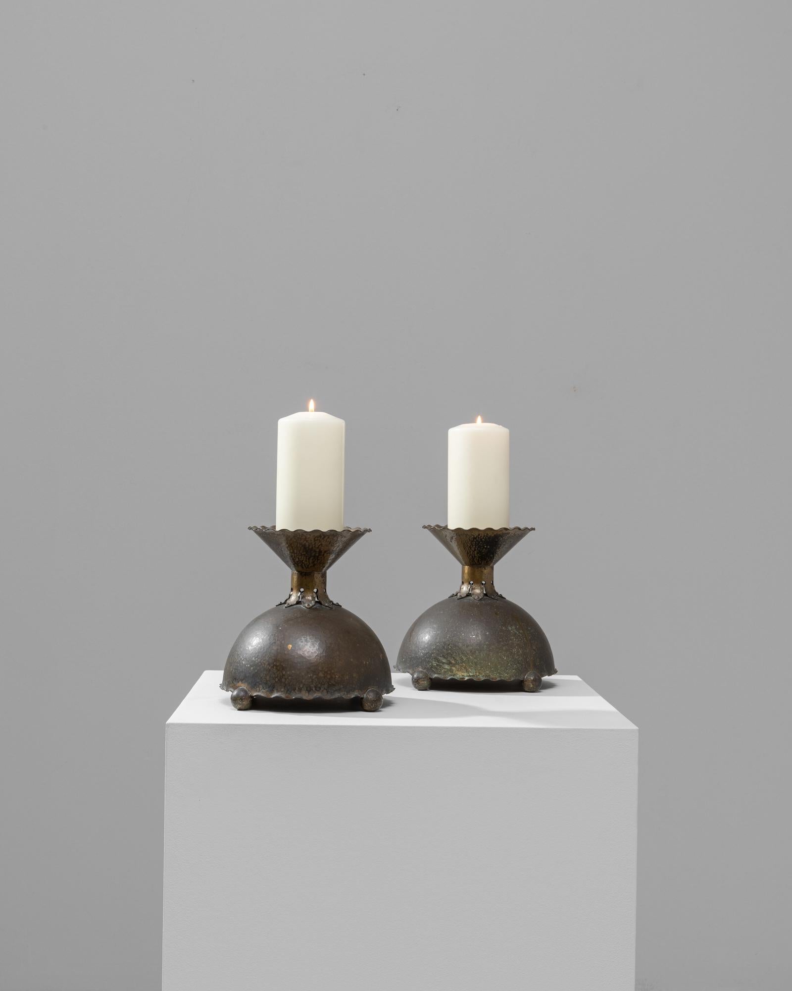 Add a touch of antique elegance to your home with this pair of early 20th-century French copper candlesticks. These distinctive pieces showcase the superb craftsmanship of the era, featuring a robust, spherical base with a beautifully patinated
