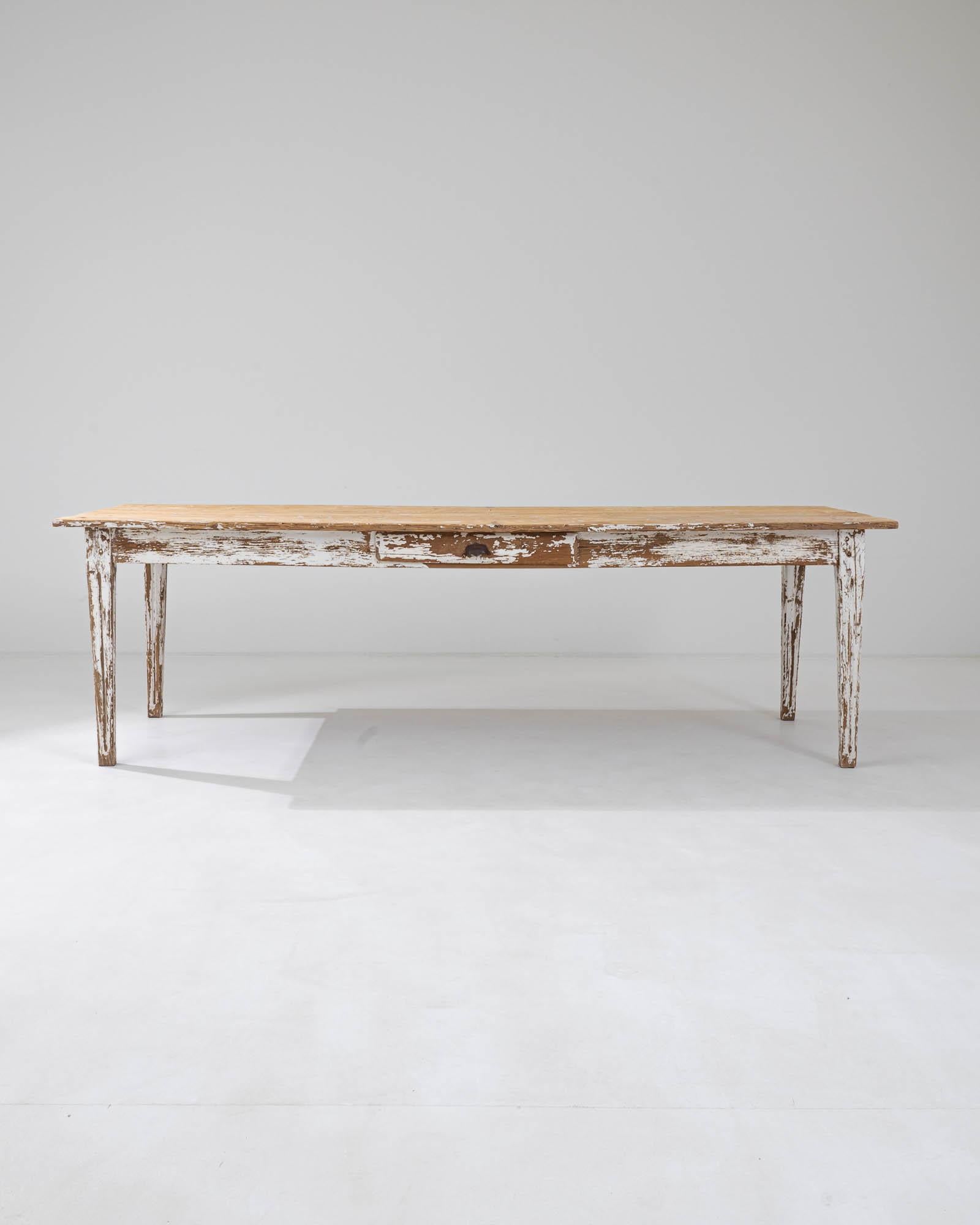 This vintage provincial dining table combines a simple shape with a homey patina for a timeless appeal. Hand-crafted in France in the early 20th century, a long rectangular tabletop sits atop an apron housing a small drawer, perfect for household