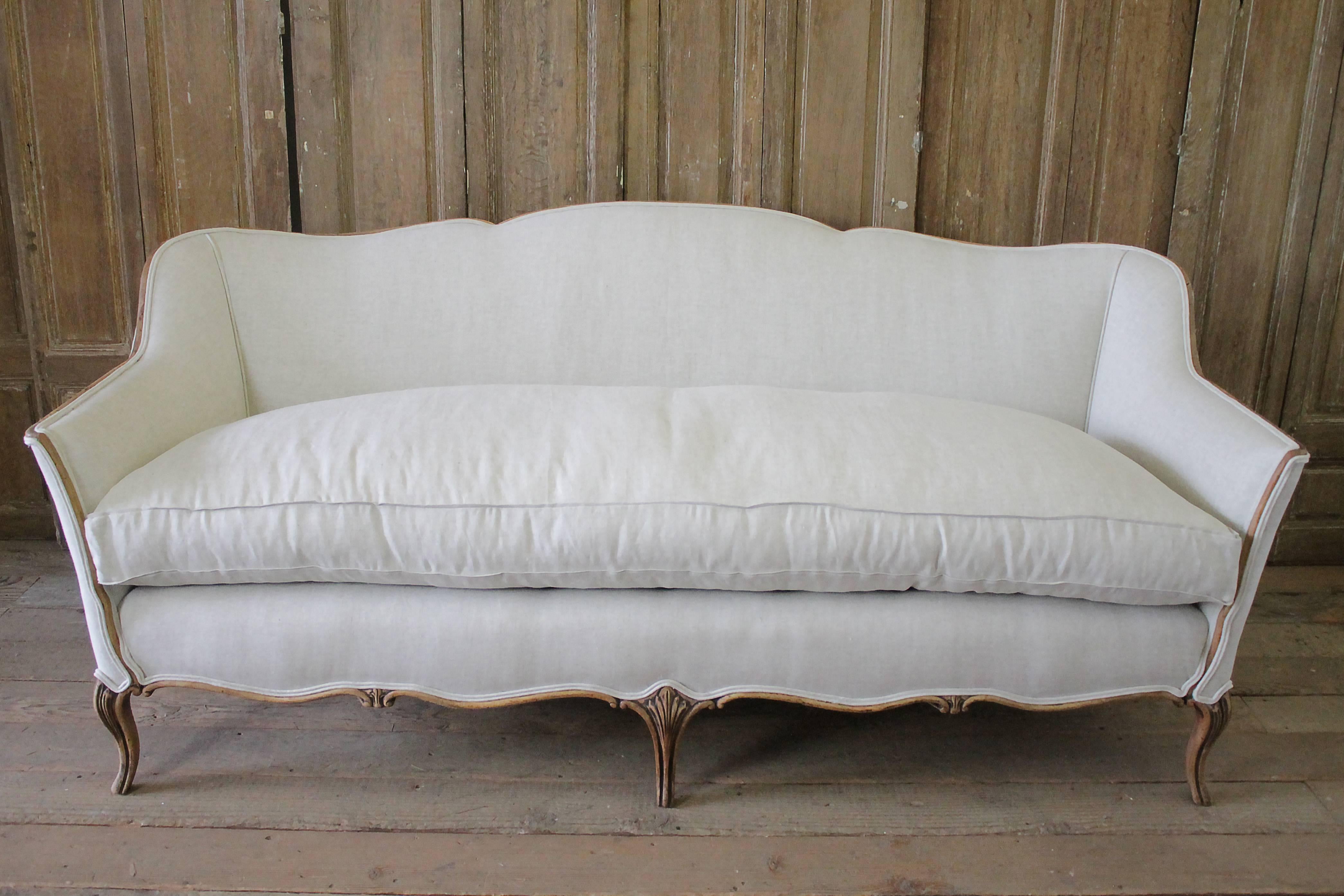 Early 20th century French country style Belgian linen upholstered sofa.
The wood frame has a wonderful stripped weathered look, great patina, medium colored walnut. Mustache back shape, we reupholstered this sofa in an oatmeal colored Belgian