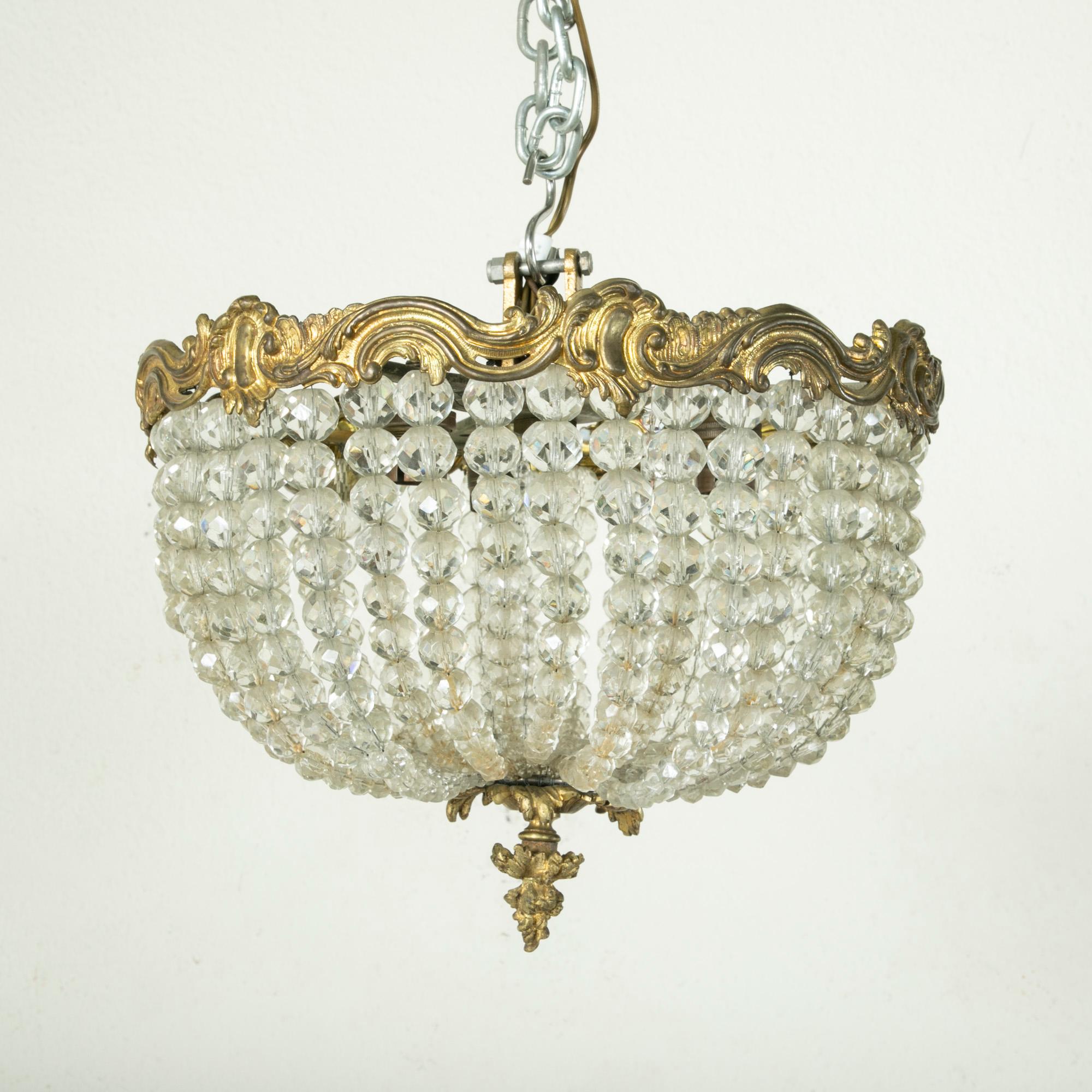 This early twentieth century French flush mount chandelier features an upper bronze ring of scrolling leaves. Multi-faceted strings of crystal beads drape to meet at a lower finial. An ideal chandelier for a powder bath or small entryway. Wired to