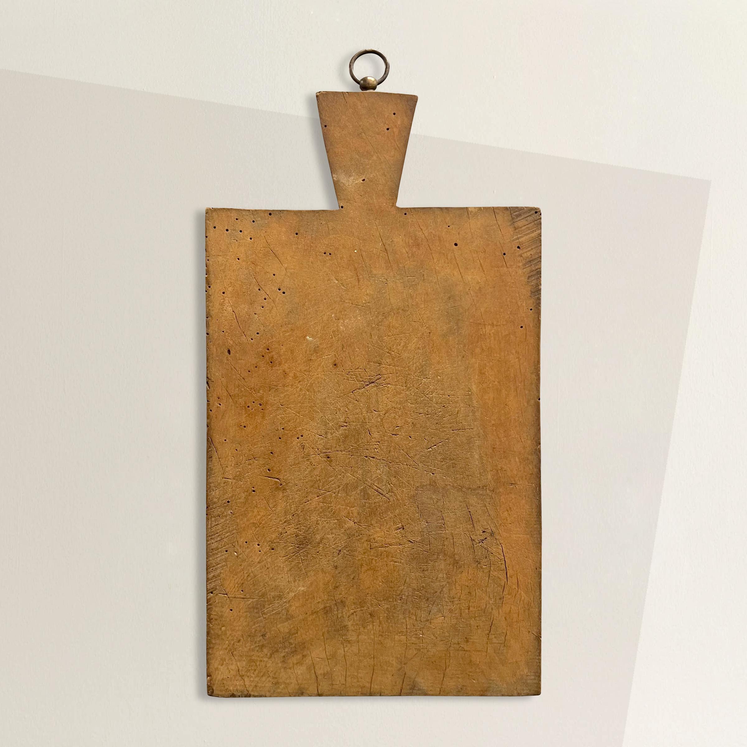 A wonderful early 20th century French cutting board with hundreds of knife marks, a brass ring for hanging, and a patina that only time can bestow. Perfect for chopping vegetables and bread, or serving cheese and charcuterie at your next fête.