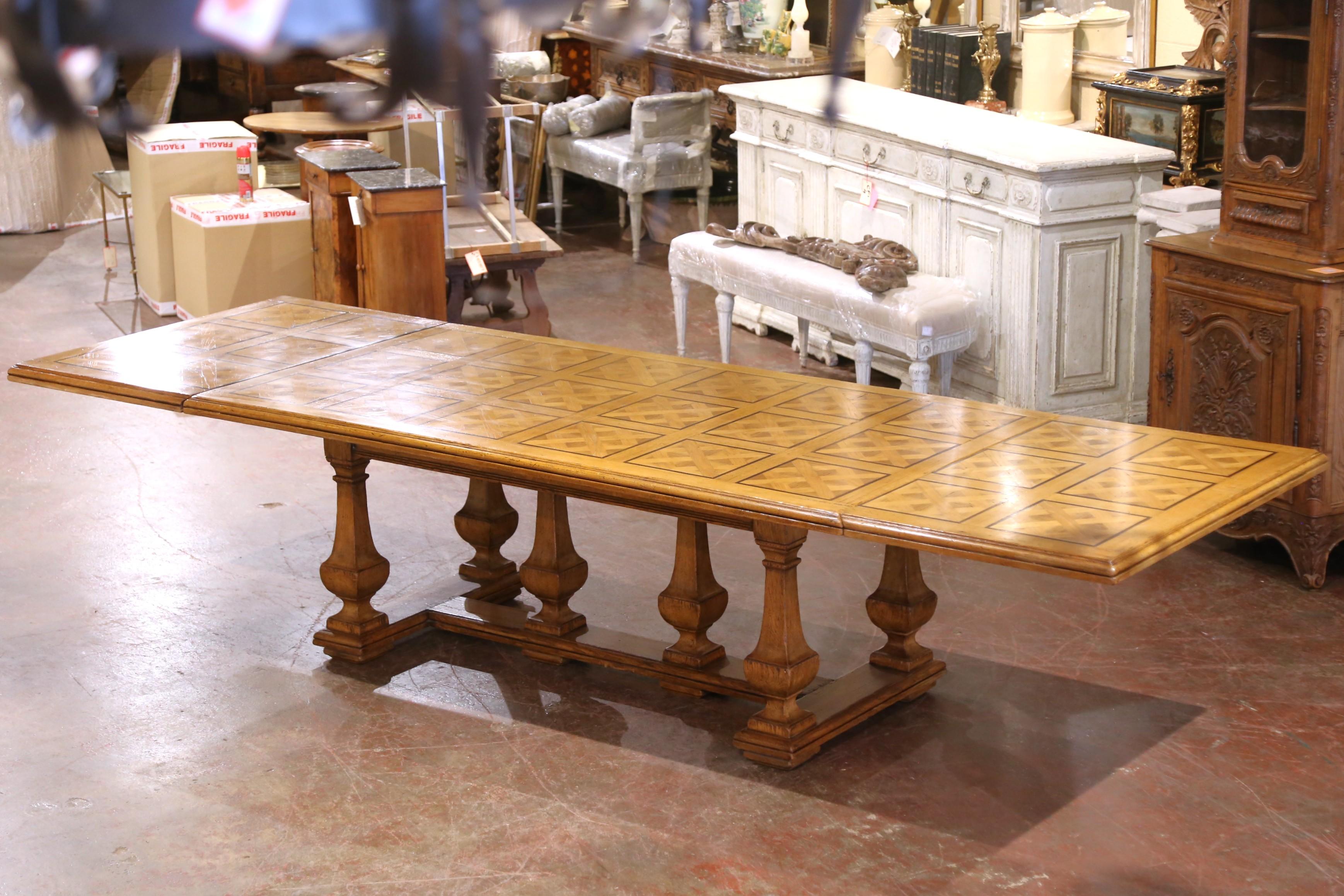 Crafted in France circa 1920, this elegant mid-century extendable dining table showcases a striking parquetry top and solid oak construction. The rectangular surface is richly inlaid with geometric diamond motifs, forming a repeating lattice pattern