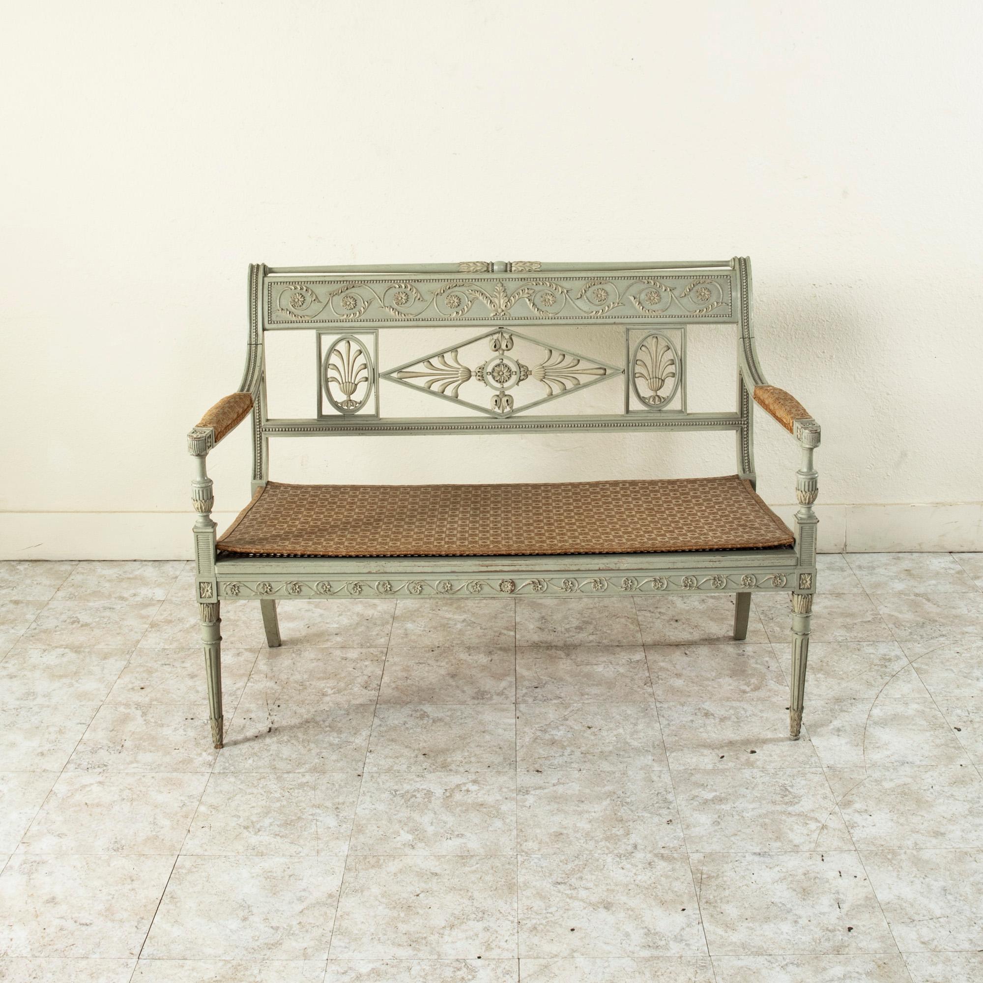 This French Directoire style banquette from the turn of the twentieth century features a scrolled seat back detailed with a carved central rosette flanked by palmettes within a classic diamond shape. The seat back is additionally detailed with