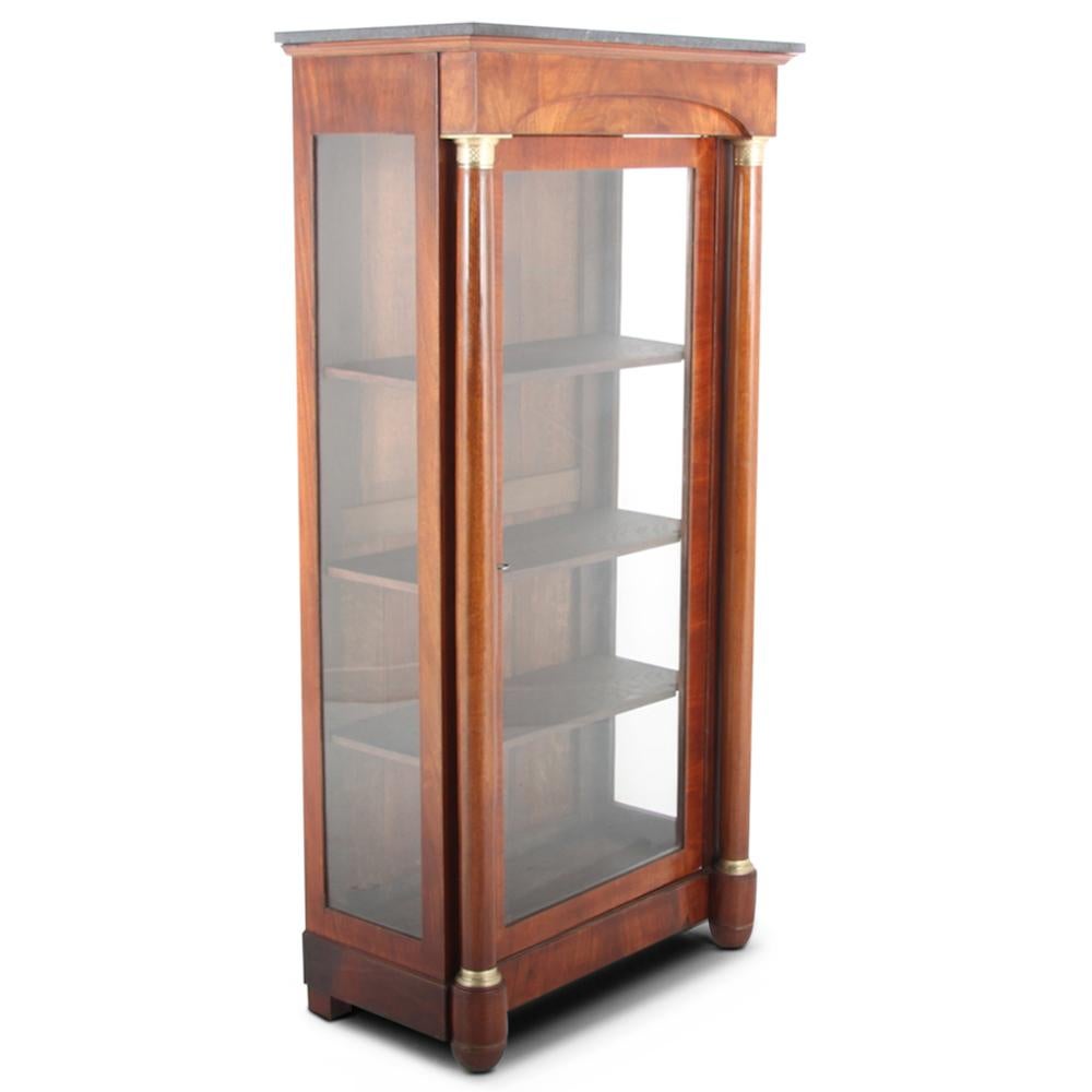 A handsome French Empire style display cabinet or ‘vitrine’ having a single full-length glass door opening to four sturdy oak shelves, and the sides with full-length glass panels. Side columns with brass bases and capitals rise to an arched pediment
