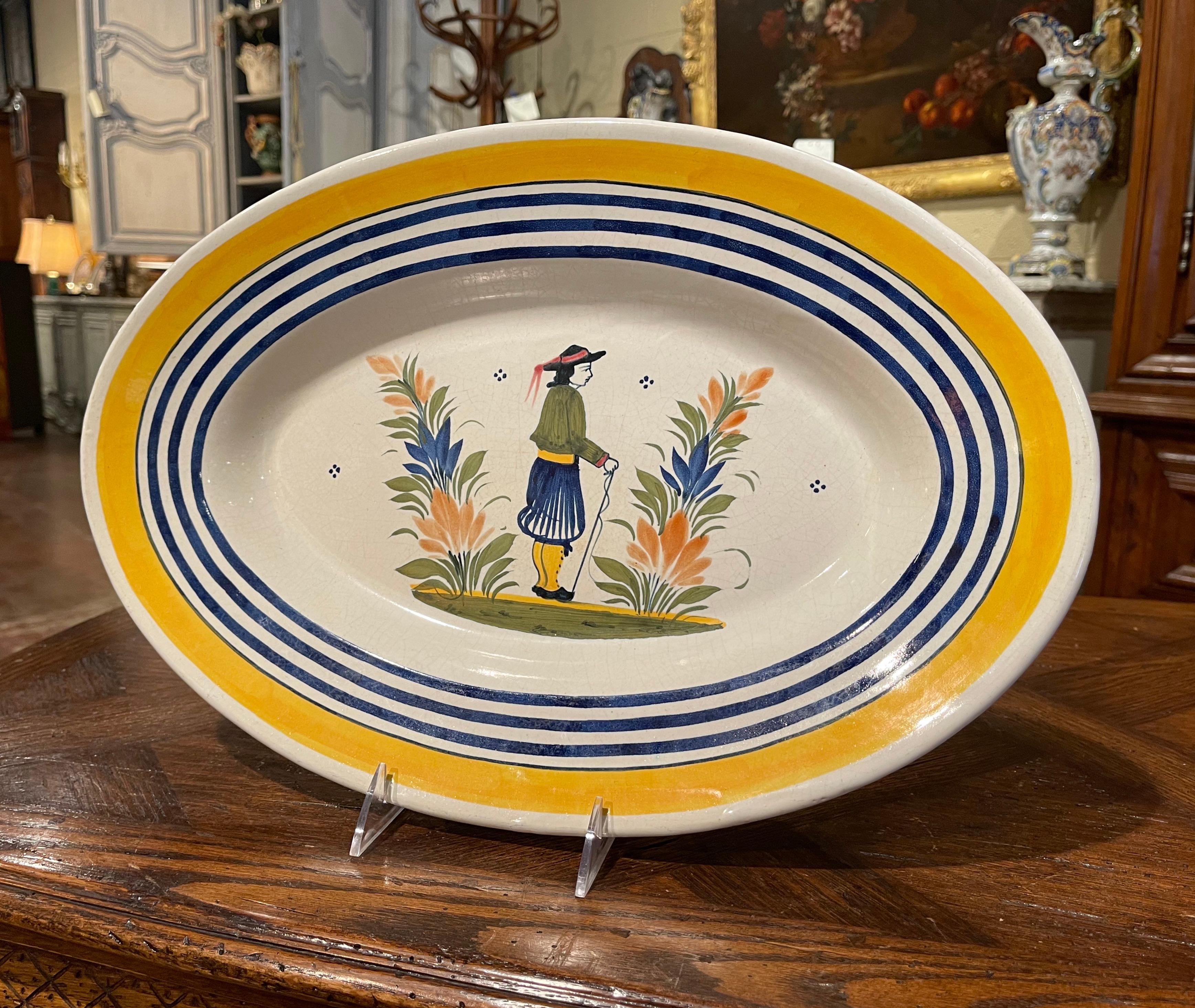 Decorate a kitchen wall or a shelf with this colorful antique decorative plate. Crafted in Brittany, circa 1920, the oval faience plate is hand painted with traditional Breton figure and foliage motif, further embellished with blue and yellow