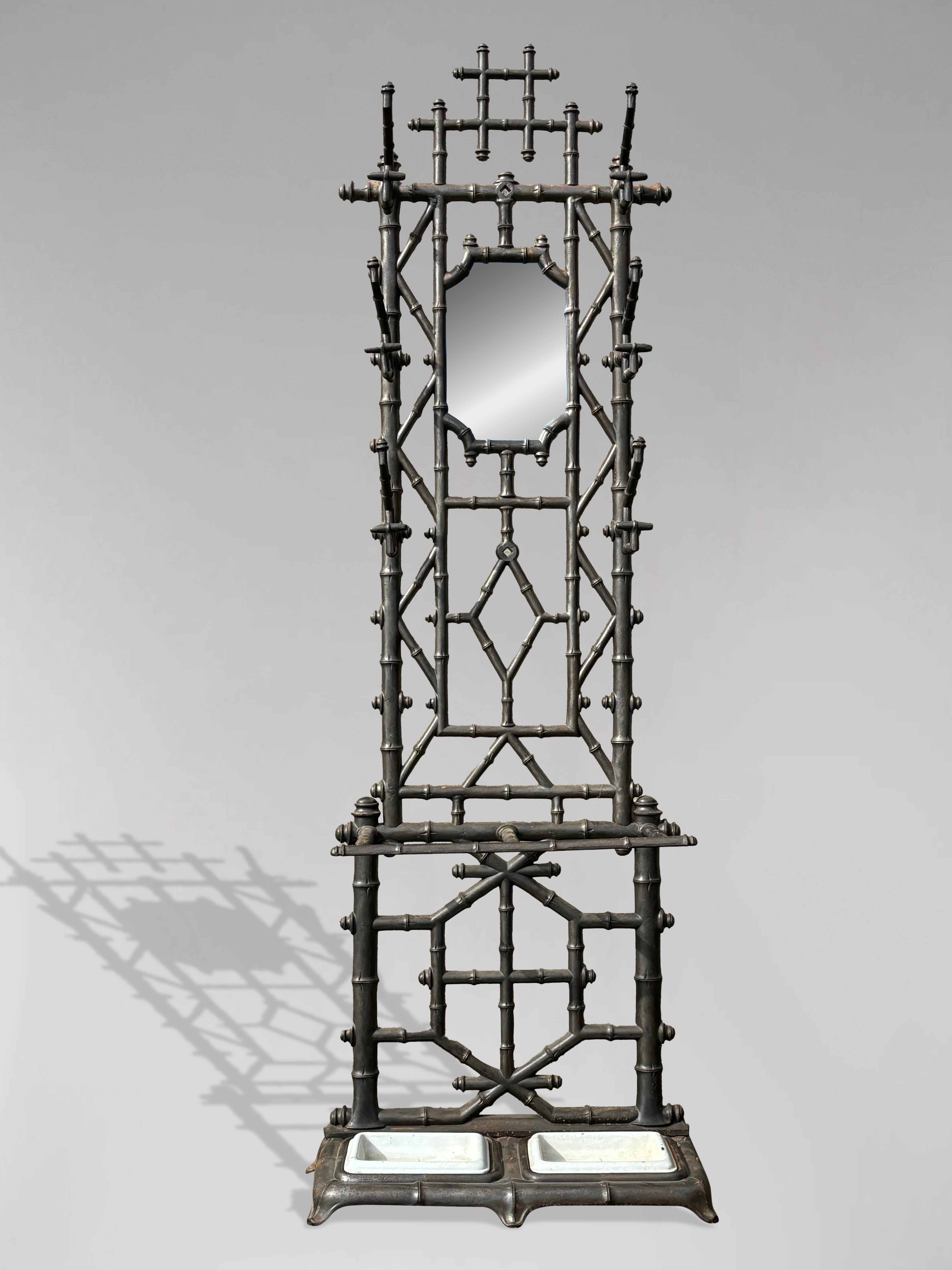 A beautiful freestanding antique French patinated cast iron hallstand or coat rack, featuring a sculptural faux bamboo motif frame. The rack includes six double hooks for coats or hats, surrounding an original antique hexagonal inset mirror. The