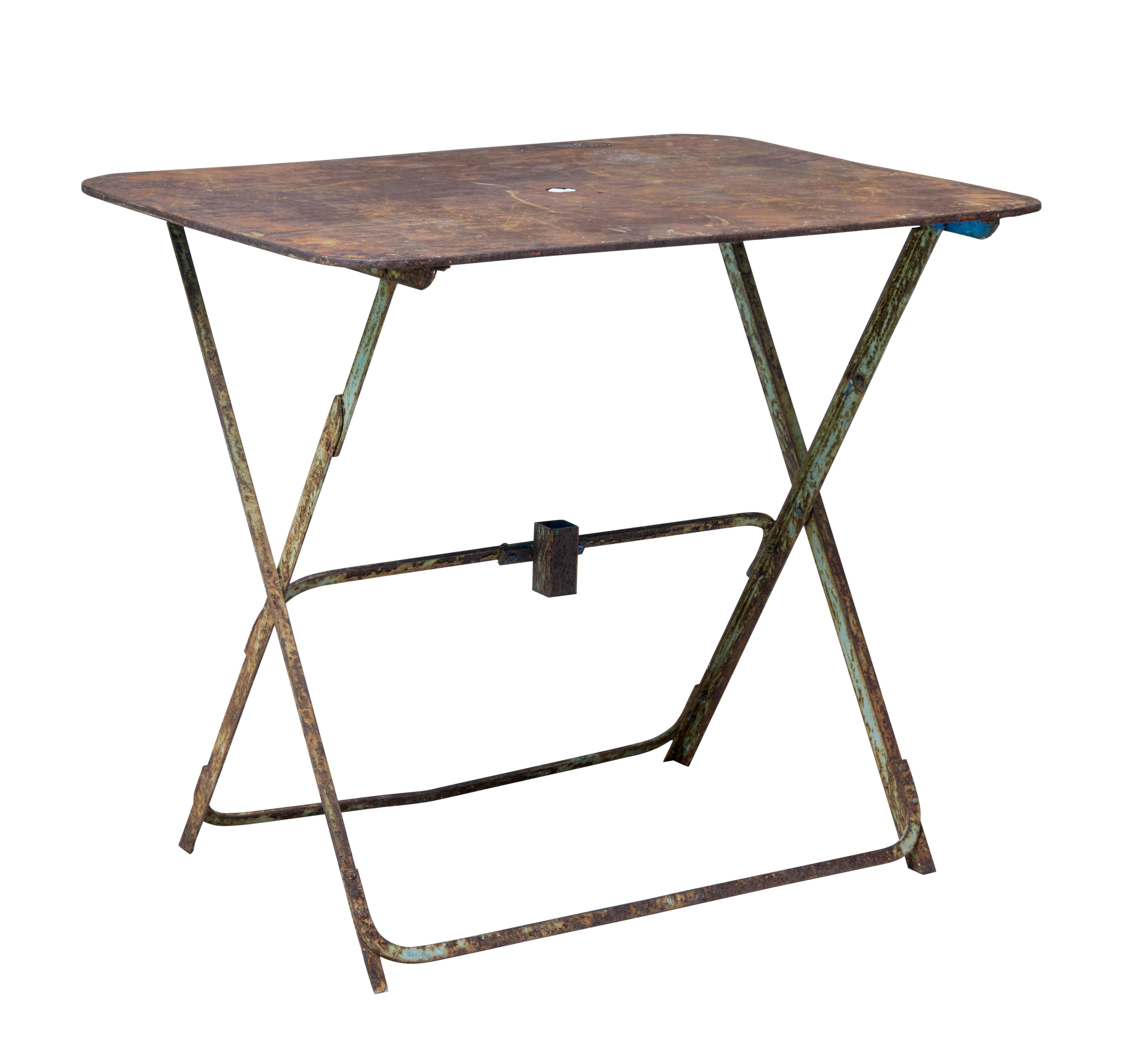 Good quality rectangular metal garden table from the 1920s.

Desirable bare rusted metal top with small parasol hole. Standing on folding base with traces of original paint.

Good example of a practical table for the garden or summer house.