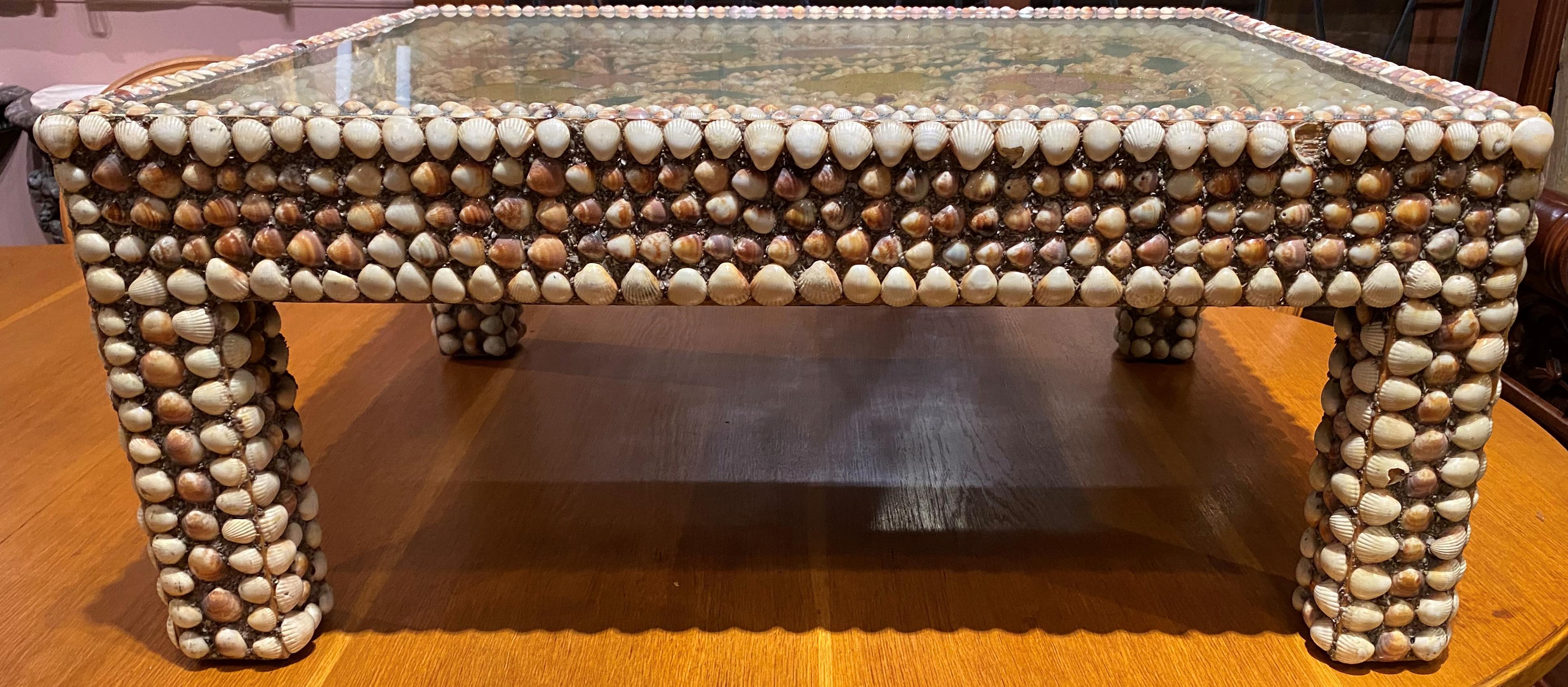 A wonderful folk art rectangular shellwork table featuring a top with foliate polychrome sand design around shells under glass, with the entire surface of the sides and legs covered with small seashells set in sand, and the underside painted green.