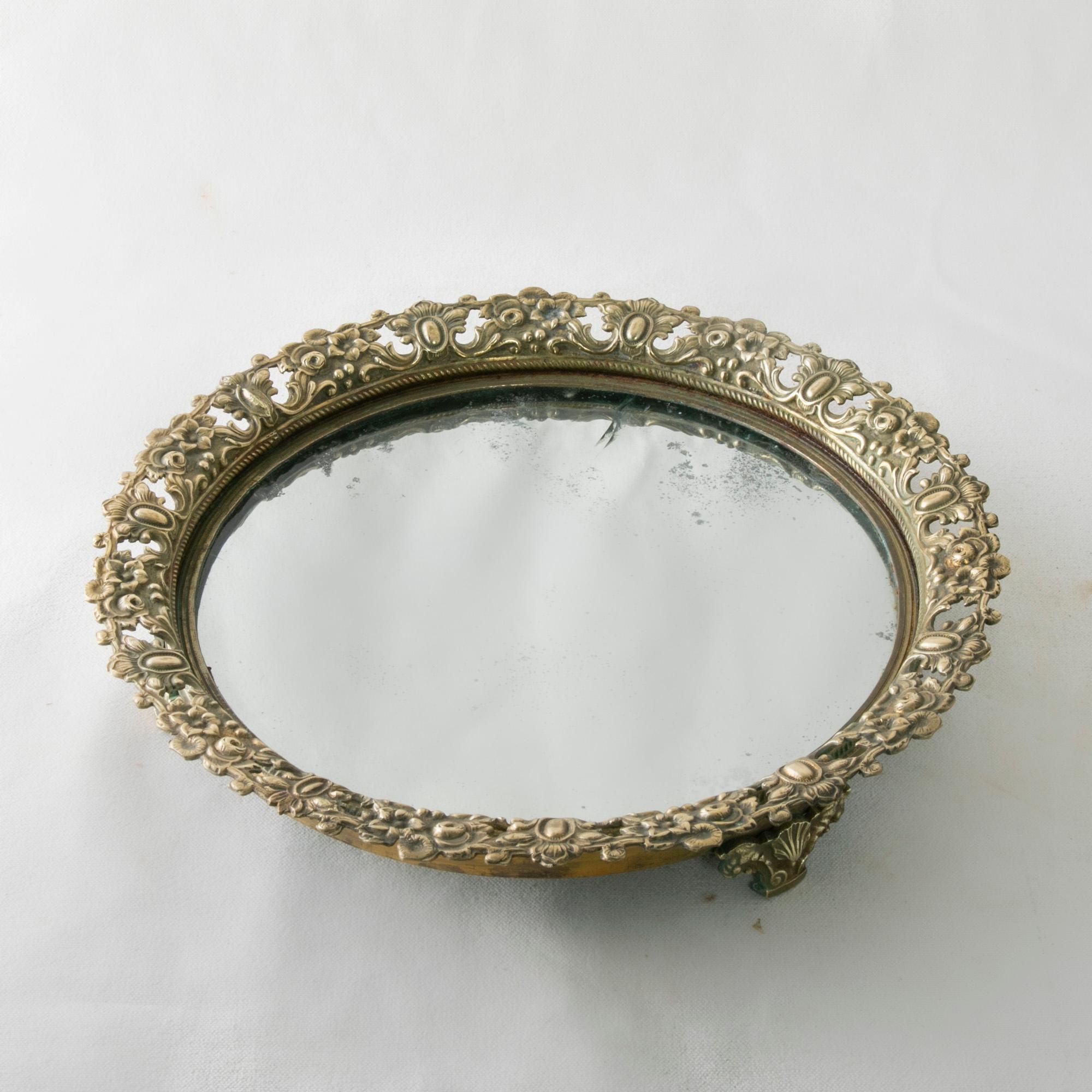 This early twentieth century French footed bronze vanity tray features a pierced gallery detailed with a floral motif. The gallery surrounds its original mercury glass mirror platform. With an 11.5 inch diameter, this oval tray would be a beautiful