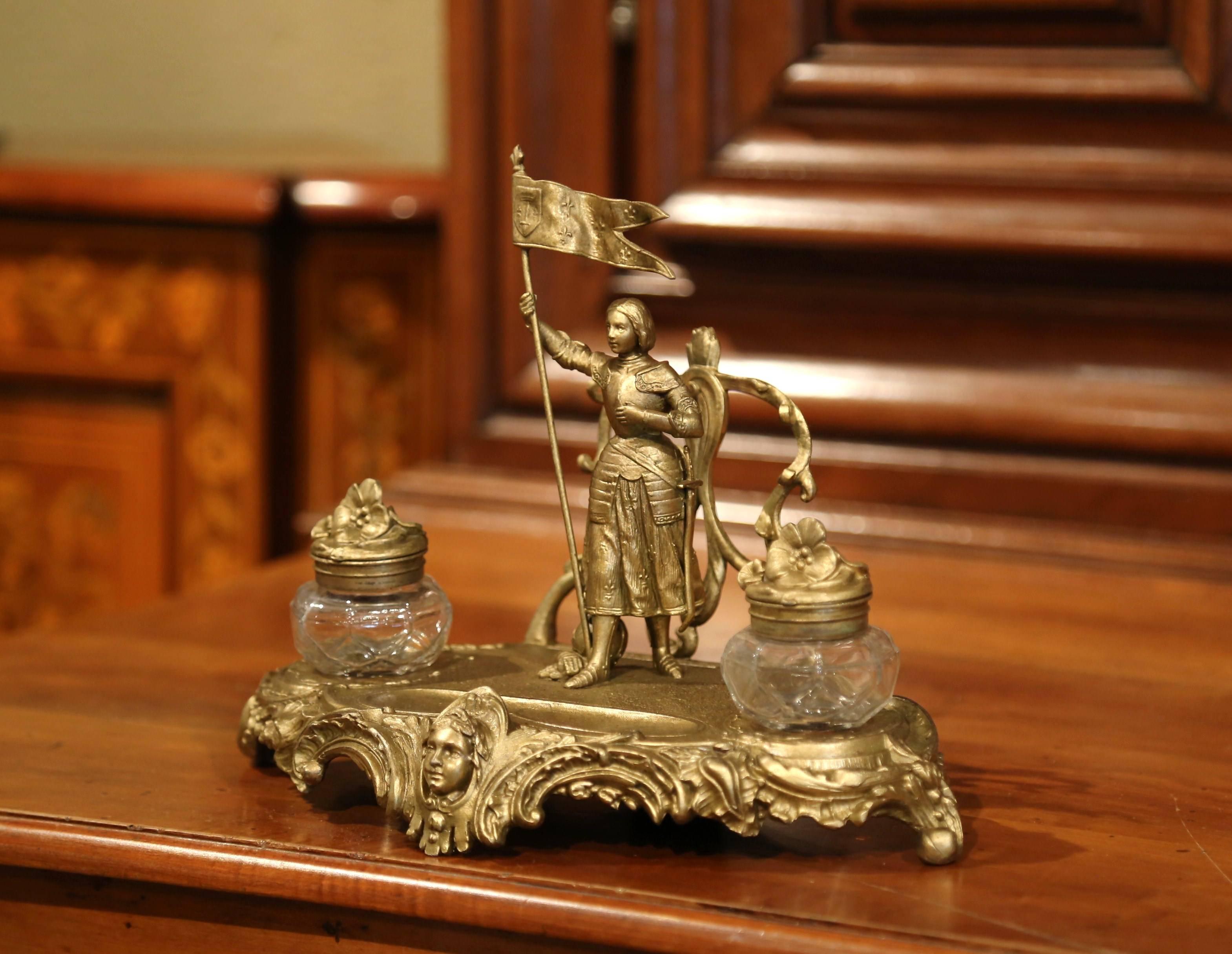 Decorate your study with this elegant antique inkwell from France. Crafted circa 1920 and made of spelter, the desk accessory stands on scrolled feet with leaf decor, and features Saint Joan of Arc standing and holding the French banner embellished