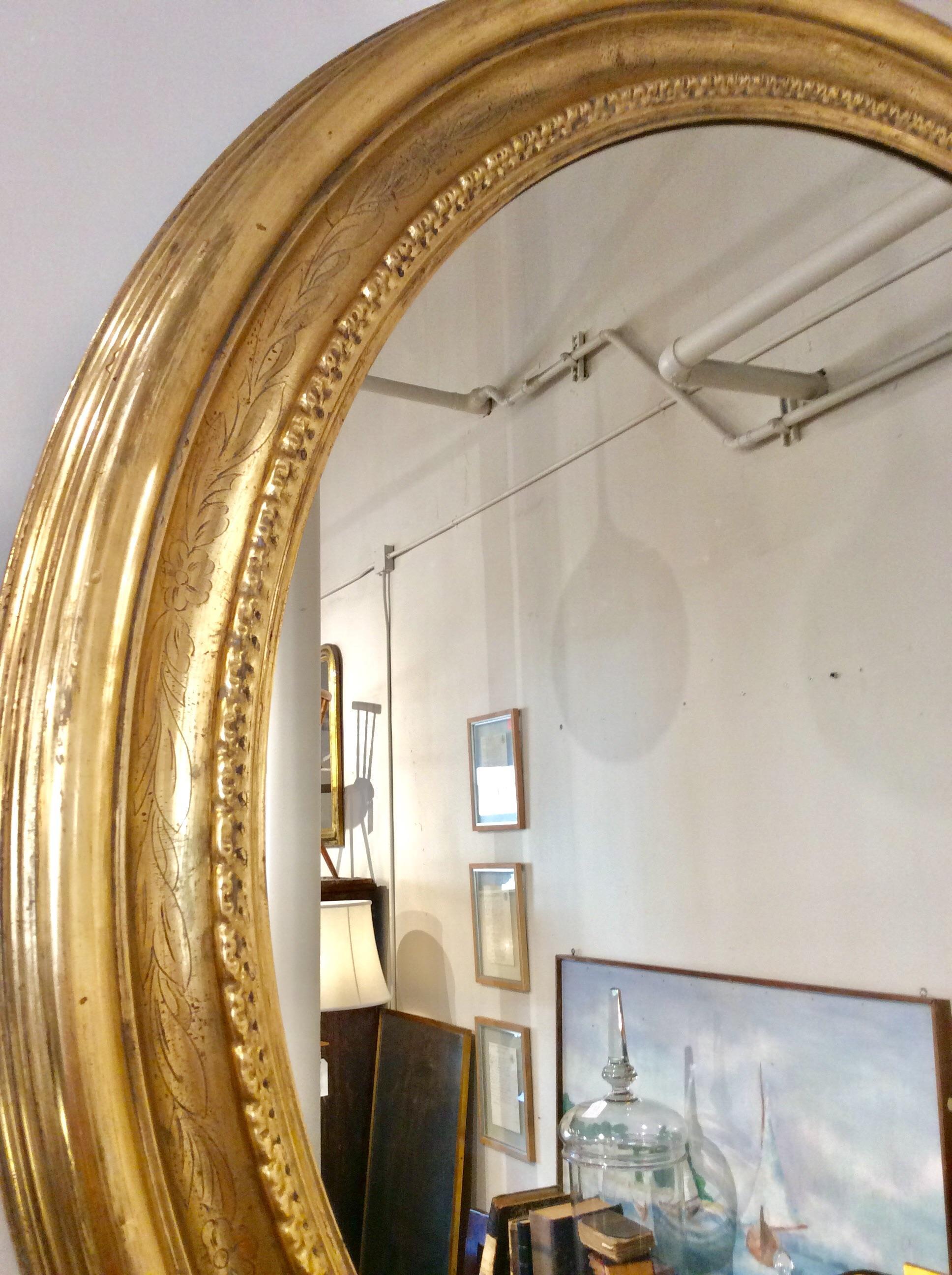 Found in France this giltwood round mirror is from the early 20th century. The large mirror features a circular giltwood frame etched with flowers and leaves. Measuring 64