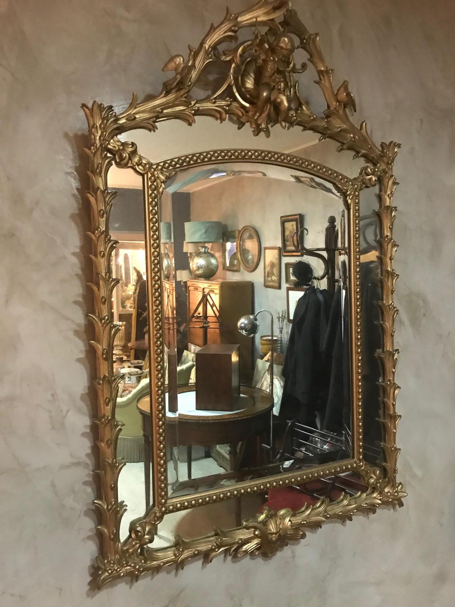 Beautiful and rare early 20th century French golden wood Louis XV mirror with an Angel holding a flower crown decoration at the top framed by two doves. 
Beveled glass in the middle. The wood has been re-painted. 
Excellent quality.
