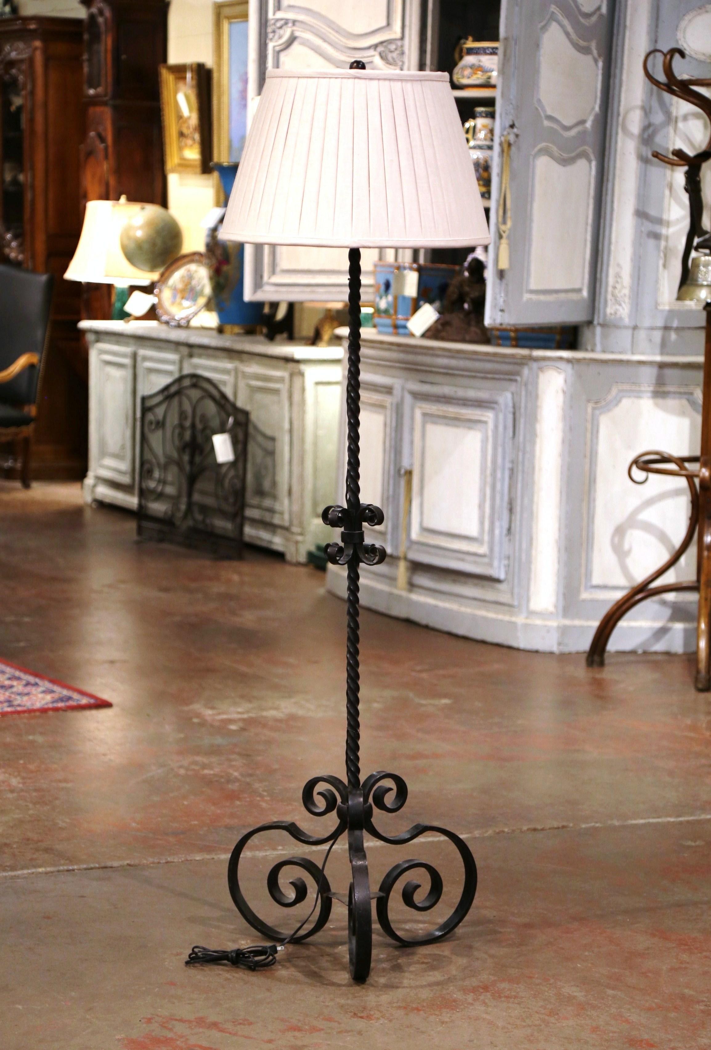 This tall iron floor lamp was created in Southern France circa 1920. Standing on a forged pedestal ending with three scrolled feet, the lamp features a twisted stem decorated with a center mount. The fixture is newly wired and is dressed with a