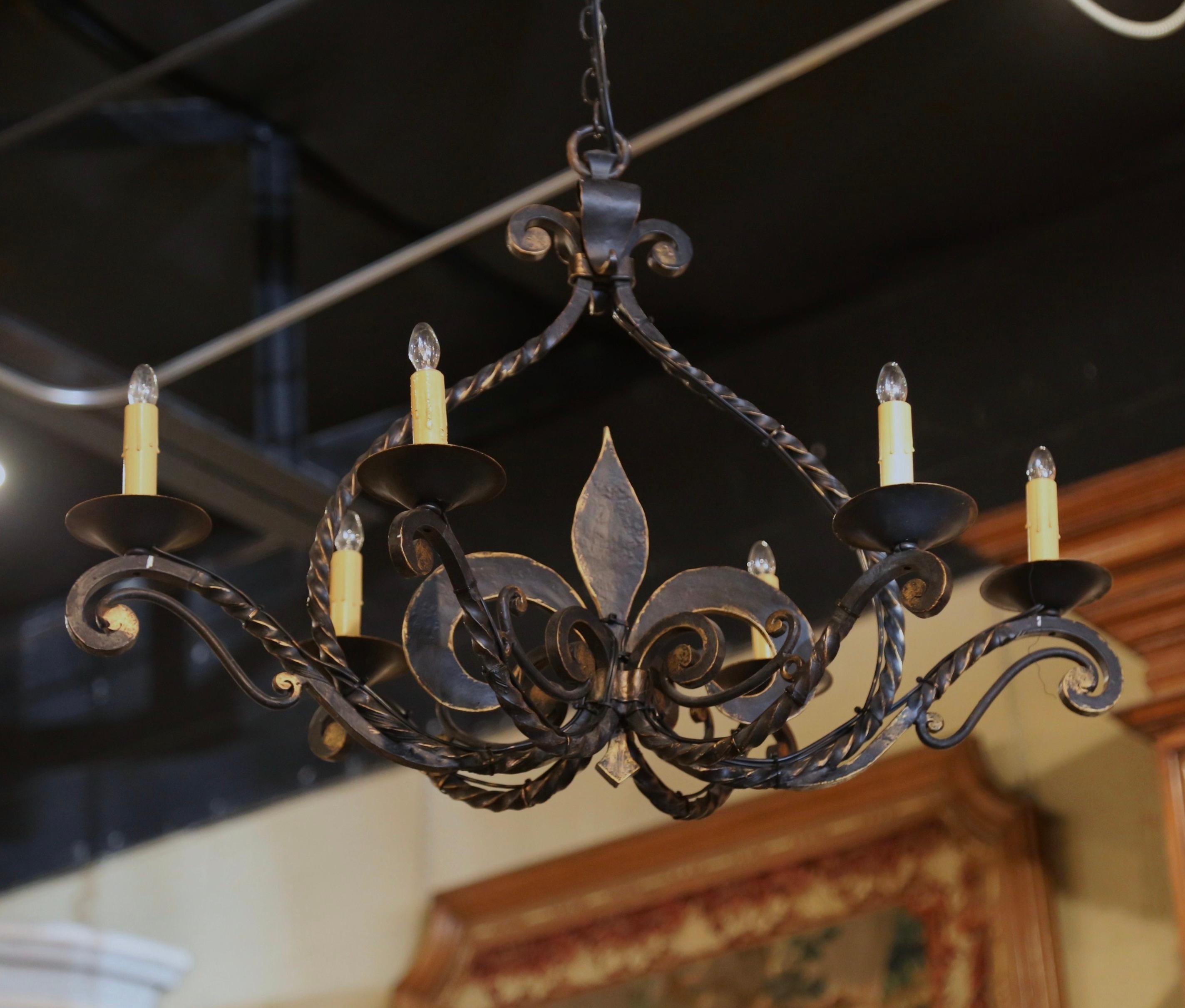 Verleihen Sie Ihrem Haus mit dieser eleganten Leuchte einen Hauch von gotischem Stil. Der antike Kronleuchter wurde um 1920 in der Normandie, Frankreich, geschmiedet und hat eine längliche Form mit einem großen, handgeschmiedeten Fleur-de-Lys-Motiv
