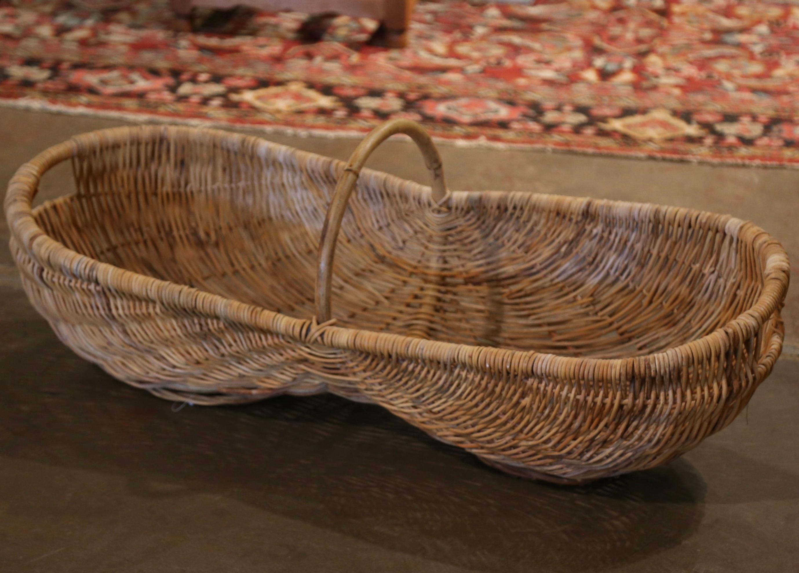Decorate a wall or a cabinet top full of flowers with this antique basket. Crafted in Normandy or Burgundy circa 1920, the large grape basket dressed with an elegant central arched bamboo handle is handwoven with wicker over a wooden frame. The kind