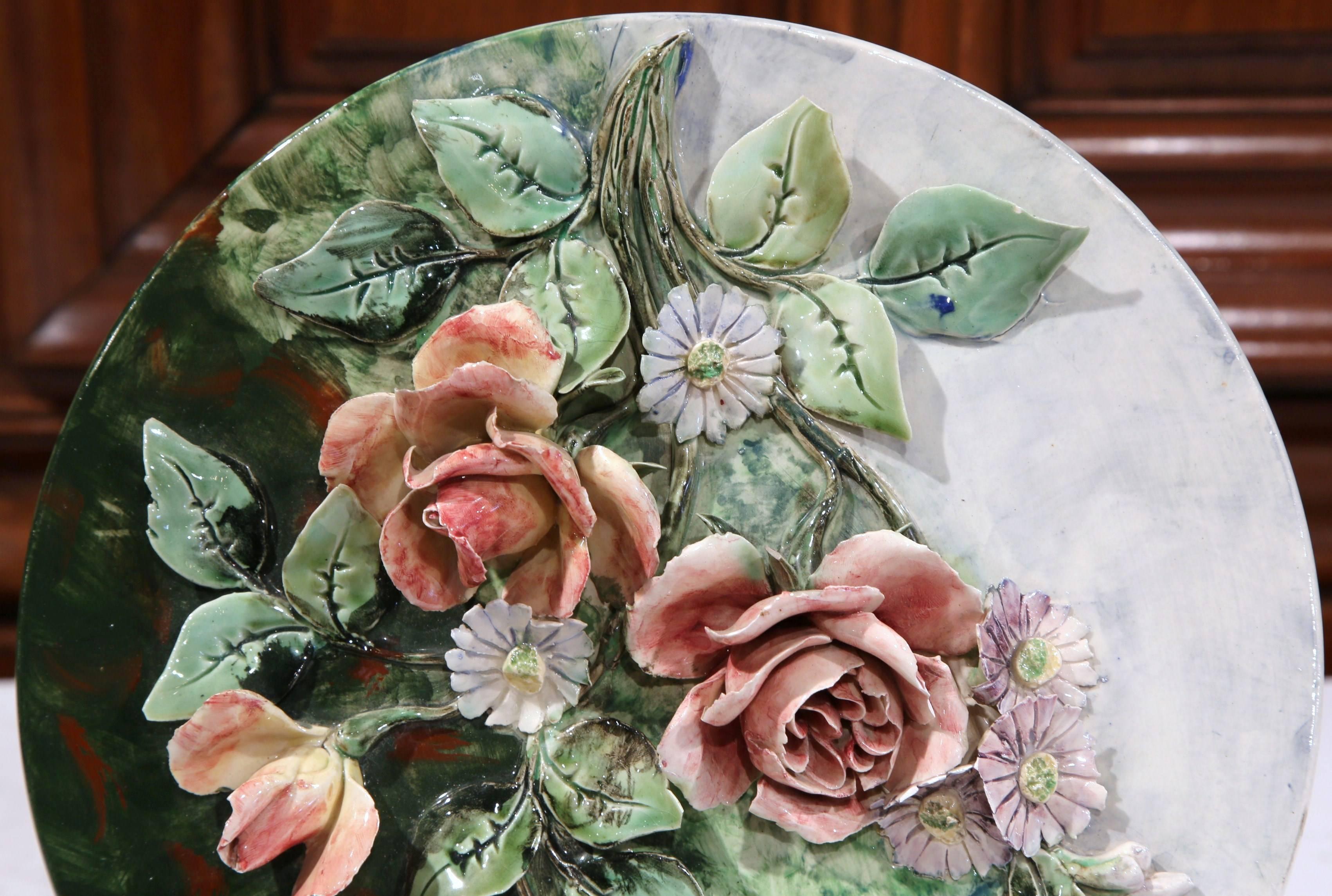 Ce classique et ancien plat à suspendre en majolique avec des fleurs a été sculpté en France:: vers 1900. L'assiette ronde en porcelaine colorée présente des roses et des tiges peintes à la main en haut-relief dans une palette de rose et de vert