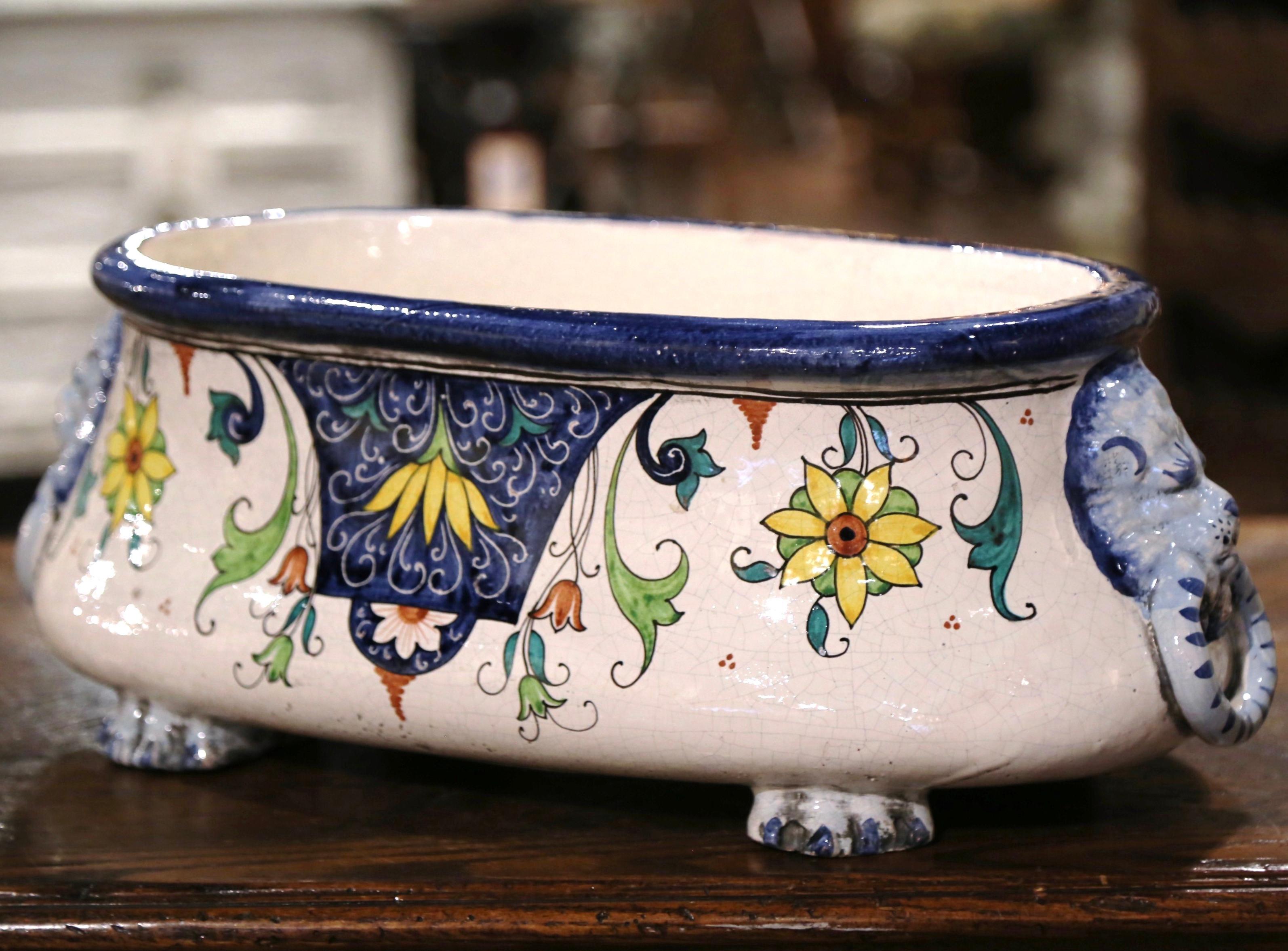 Decorate a buffet or dining table with this colorful ceramic cache pot. Crafted in France, circa 1920 and oval in shape, the jardinière stands on four paw feet and is dressed with lion head form handles. The faience planter is decorated with hand