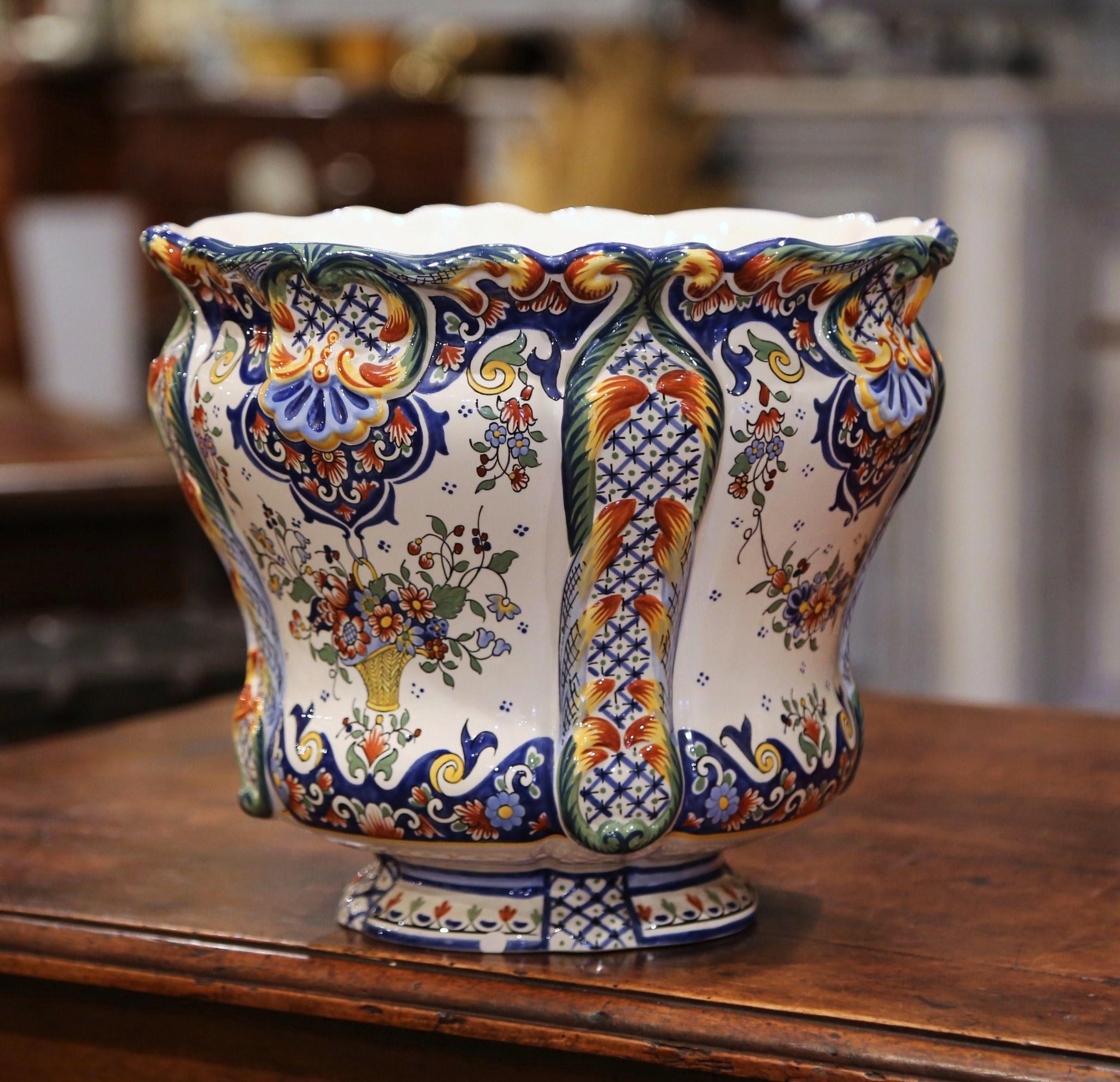 Cet élégant cache-pot antique en céramique a été fabriqué en Normandie, en France, vers 1920. De forme ronde, la jardinière classique et colorée est dotée d'un bord festonné et bouclé. Le grand bac profond en porcelaine présente un décor floral