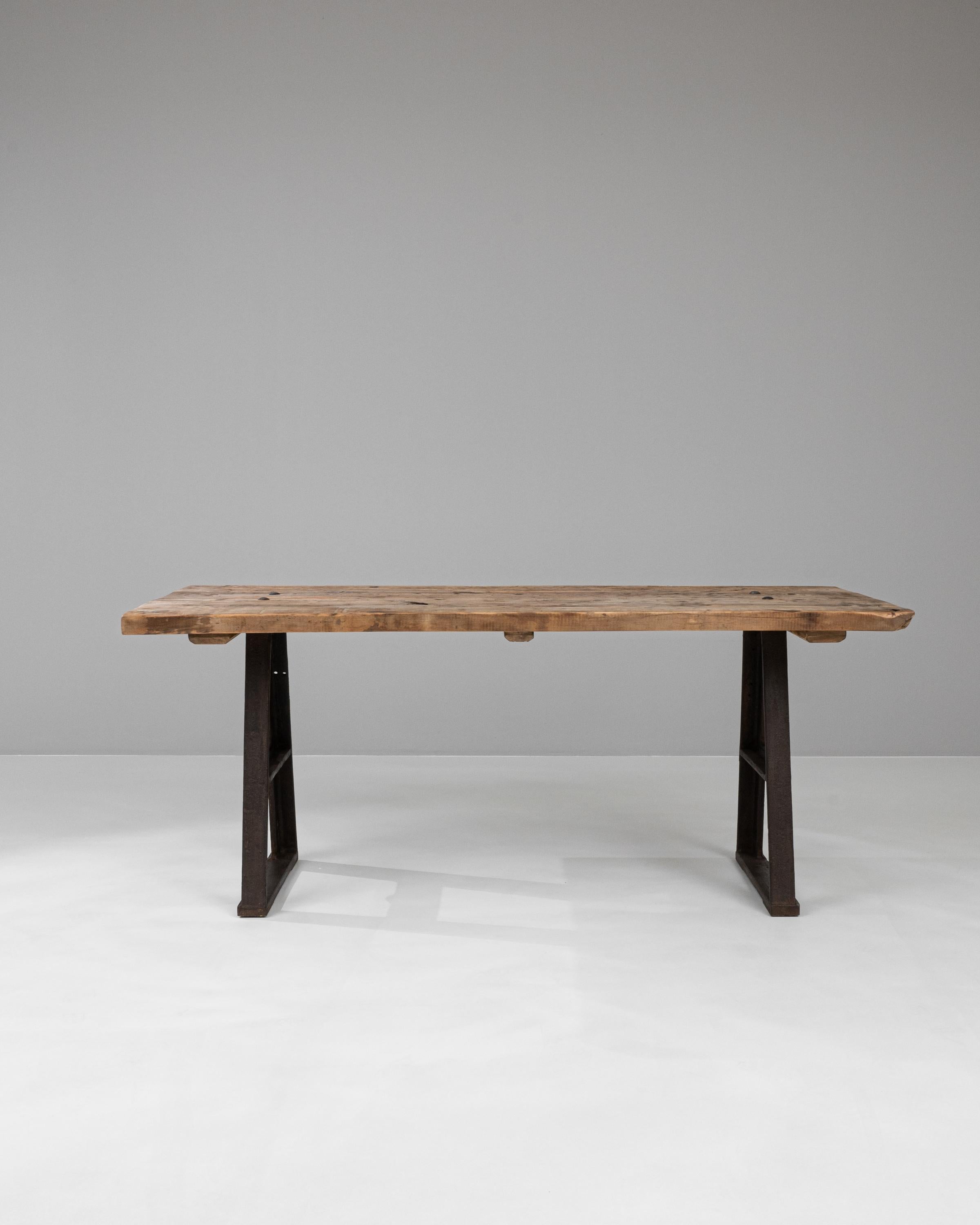 This Early 20th Century French Industrial Table is a splendid representation of utilitarian design fused with rustic charm. Its robust, dark iron legs flaunt a unique A-frame shape, indicative of the industrial era's focus on strength and