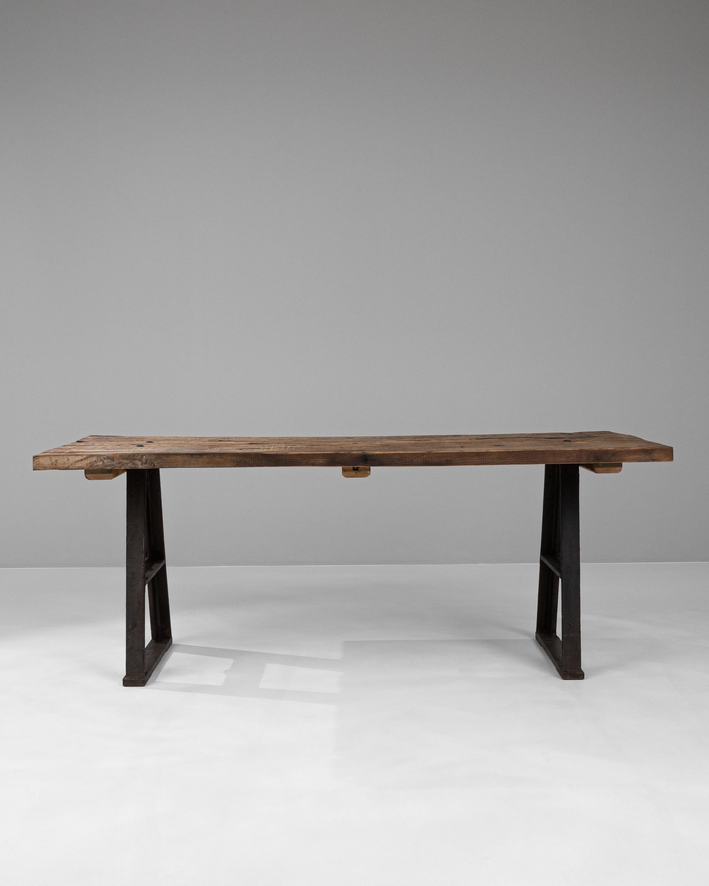 This Early 20th Century French Industrial Table is a splendid representation of utilitarian design fused with rustic charm. Its robust, dark iron legs flaunt a unique A-frame shape, indicative of the industrial era's focus on strength and