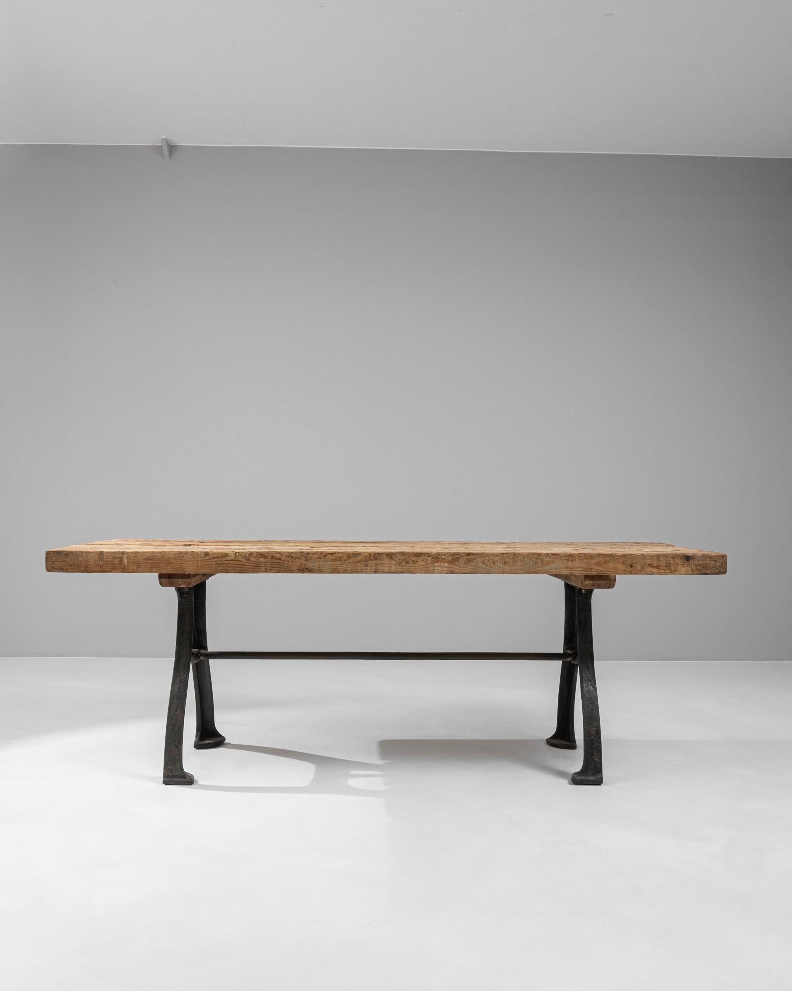 This early 20th-century French industrial table exemplifies the fusion of rugged functionality and aesthetic grace. The table features a solid, thick wooden top, rich with the character of well-worn wood, showing distinctive grain patterns and a