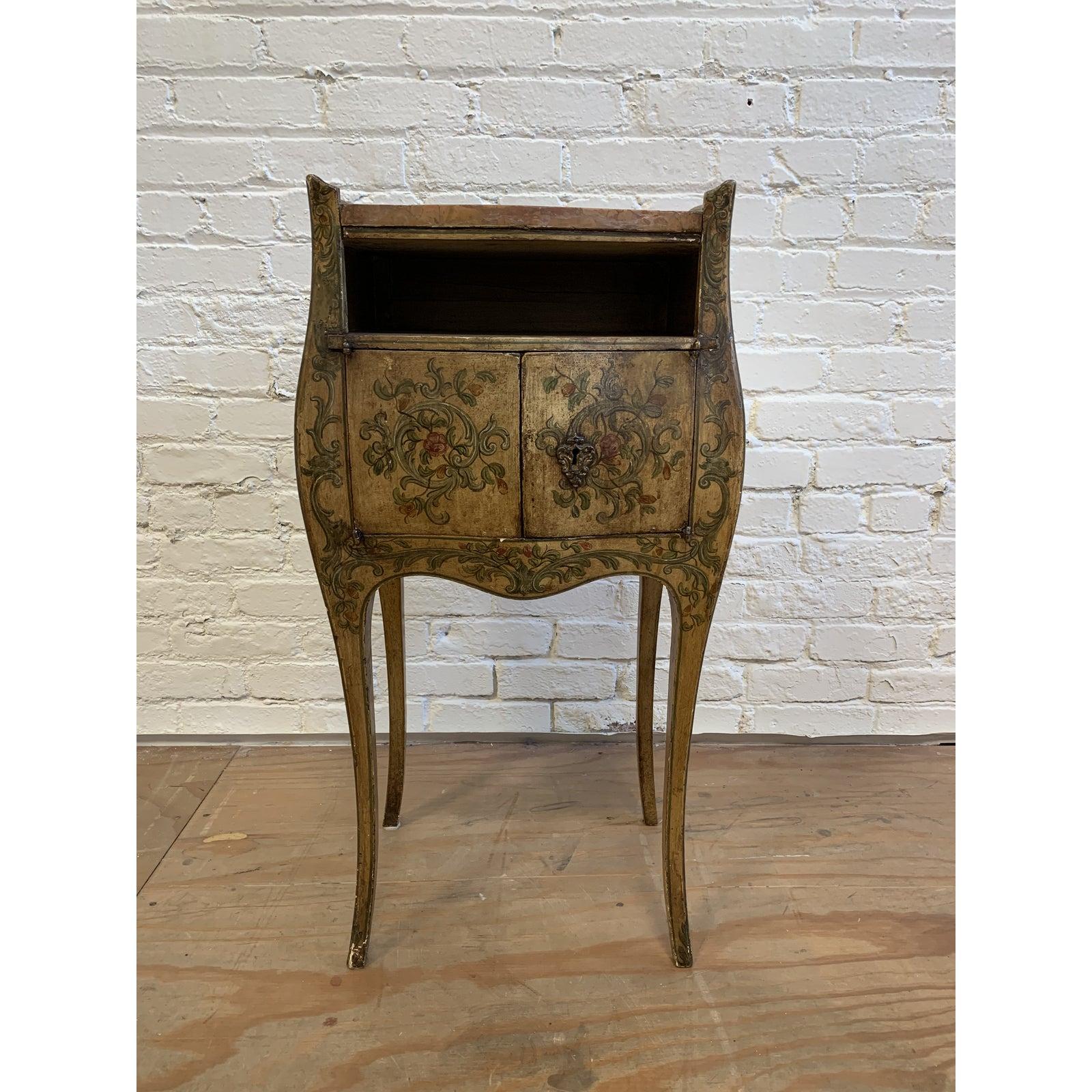A French inspired hand painted side cabinet and marble top. Floral and vine motifs surround the curvy antiqued frame. Doors reveal open storage inside and adorn brass keyhole (key not included.) Marble top in addition to frame have visible wear and