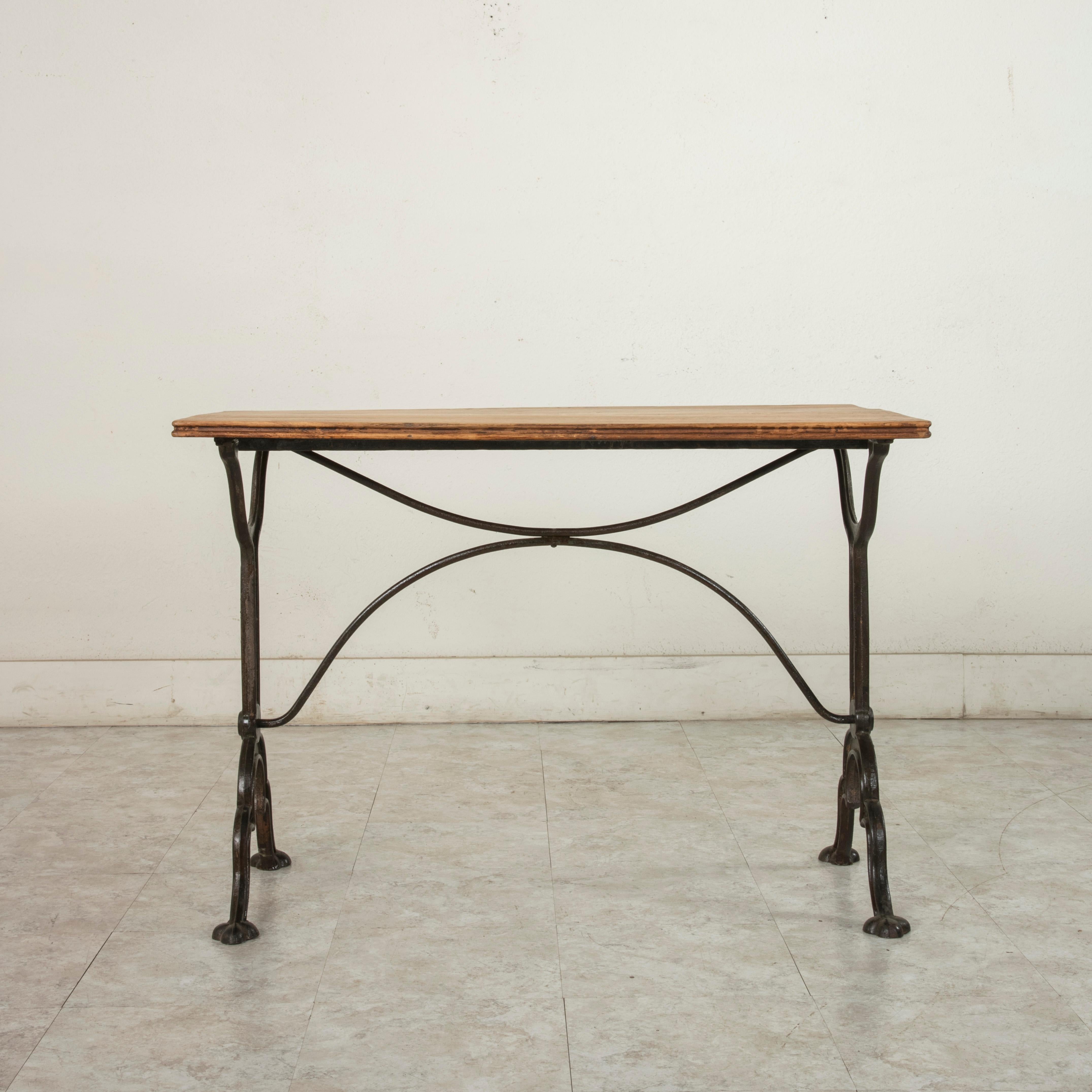 This early 20th century French bistro table or cafe table features a cast iron base and an oak top with a double beveled edge. The base is marked by the maker, Pierre Ouvrier, Paris, E. Ringuet, and the word, depose, which translates trademarked in