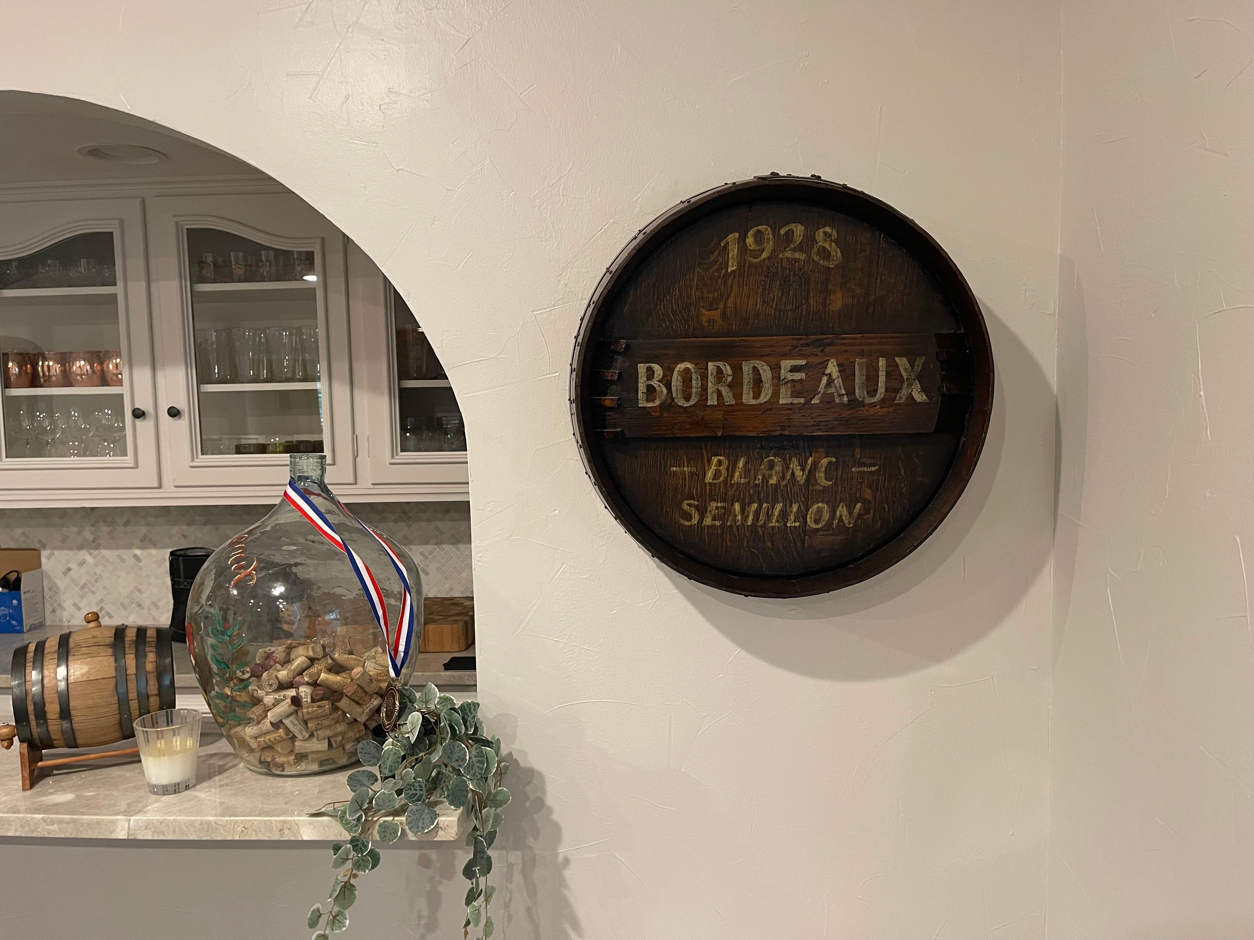 Decorate a wine cellar with this large antique wine barrel. Created in the wine Bordeaux region of France and dated 1928, the decorative piece a wine barrel top made of oak and strapped with the original metal; the round top is embellished with