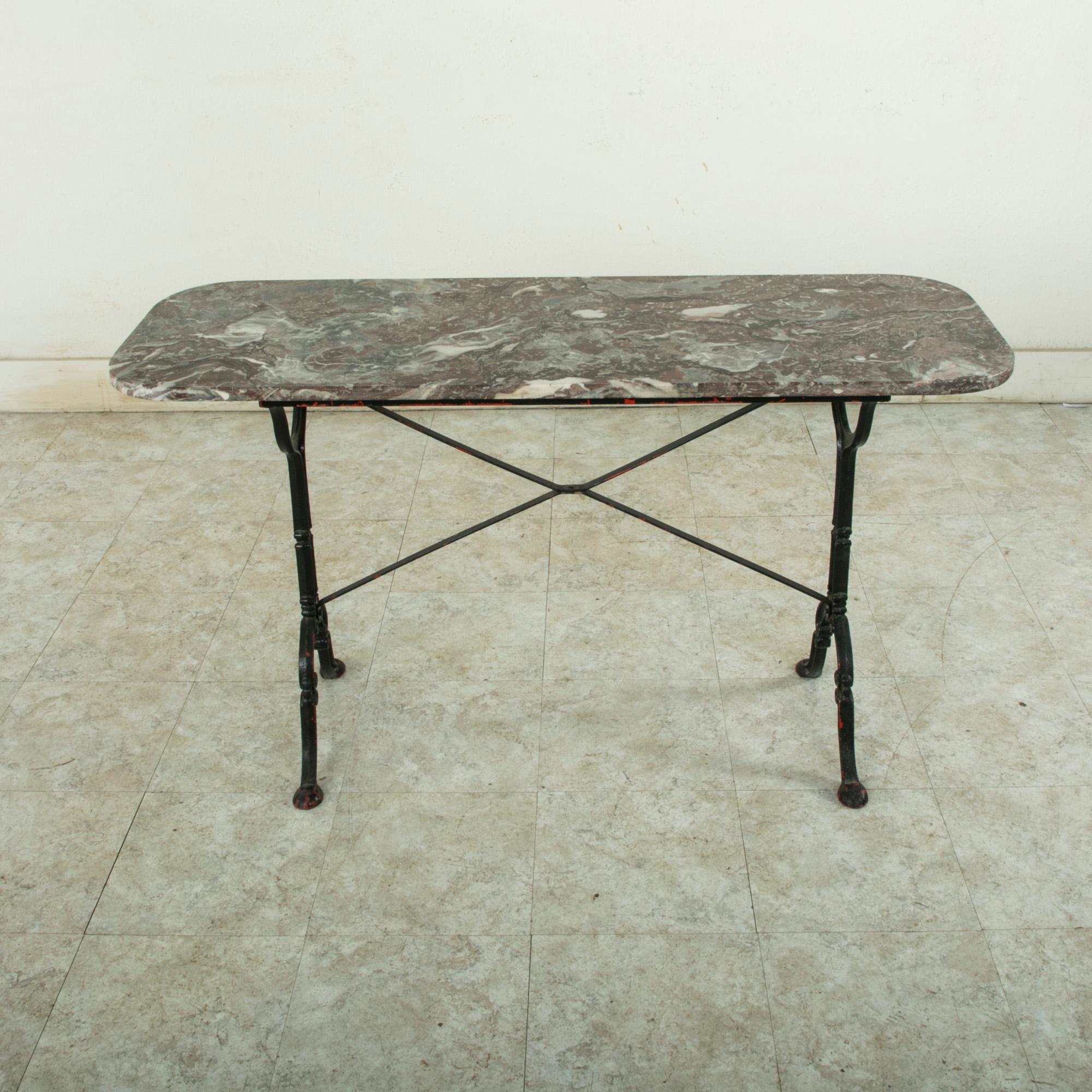Originally used in a French brasserie during the early 20th century, this cast iron bistro table or cafe table features a solid grey, white, and rose colored marble top. Scrolled iron legs support the top and are joined by an X-stretcher that