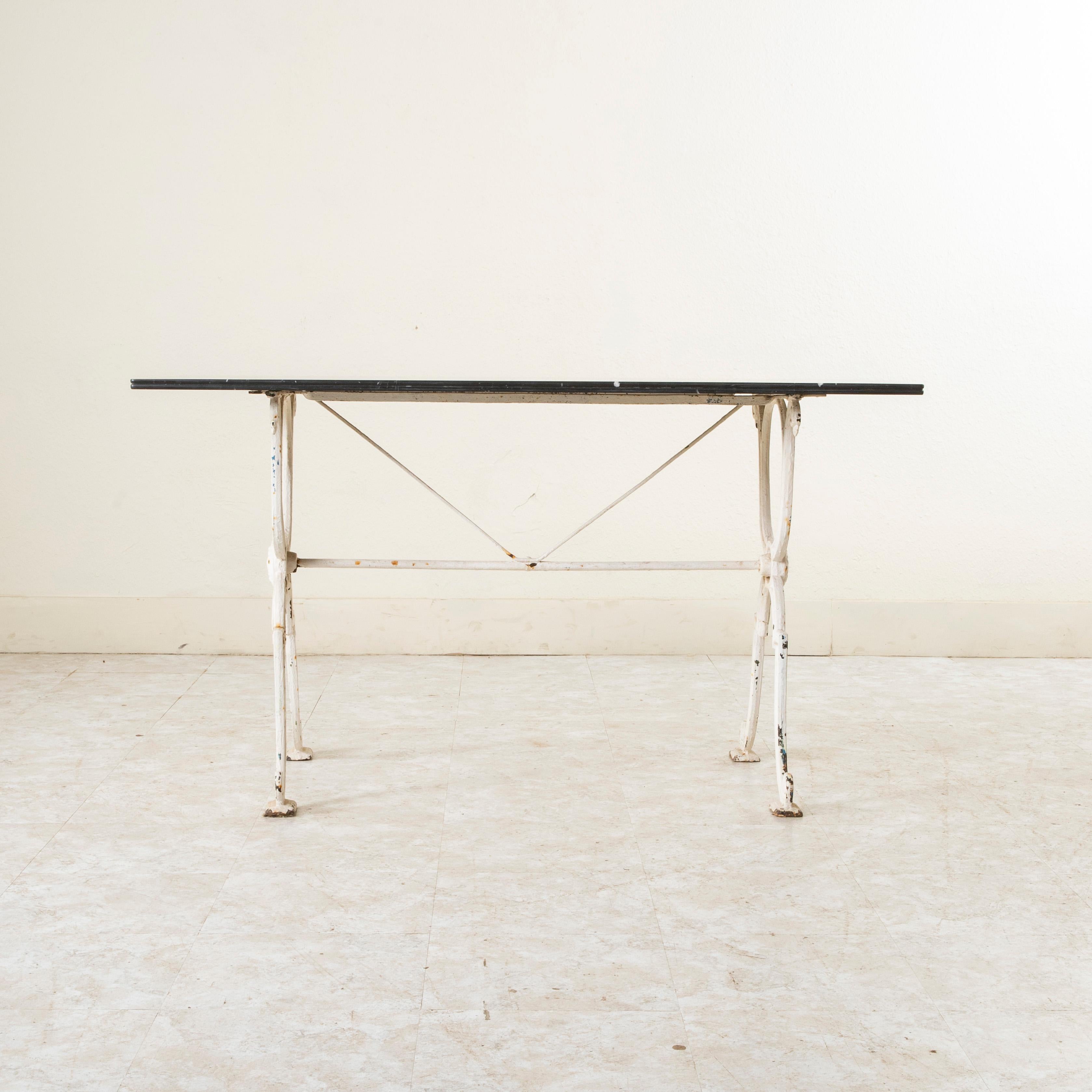 Originally used in a French brasserie at the turn of the twentieth century, this long cast iron bistro table or cafe table features a black marble top with white veining. Scrolled iron legs support the top and are joined by a stretcher capped with a