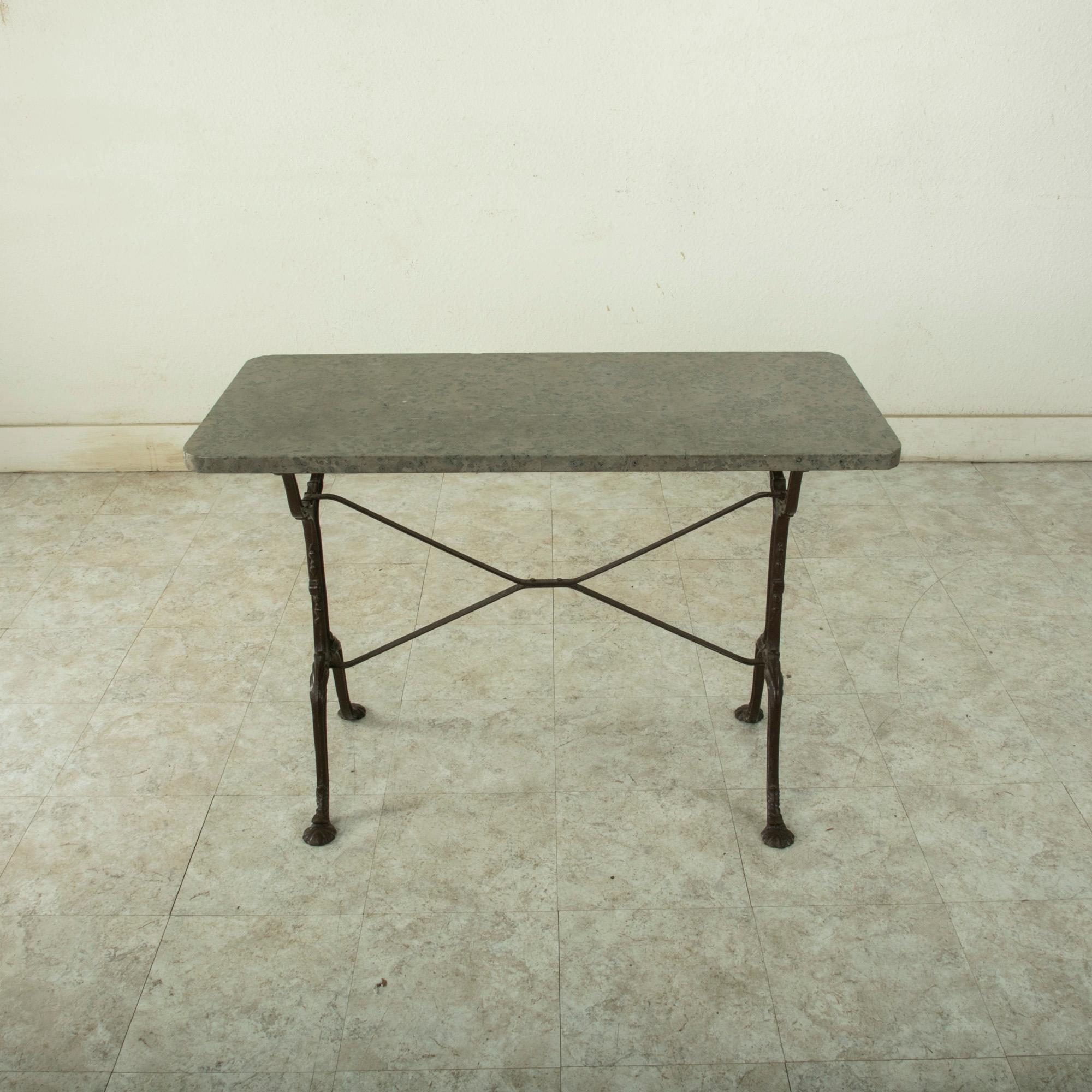 Originally used in a French brasserie during the early-twentieth century, this cast iron bistro table or cafe table features a solid grey marble top. Scrolled iron legs support the top and are joined by an X-stretcher that provides additional