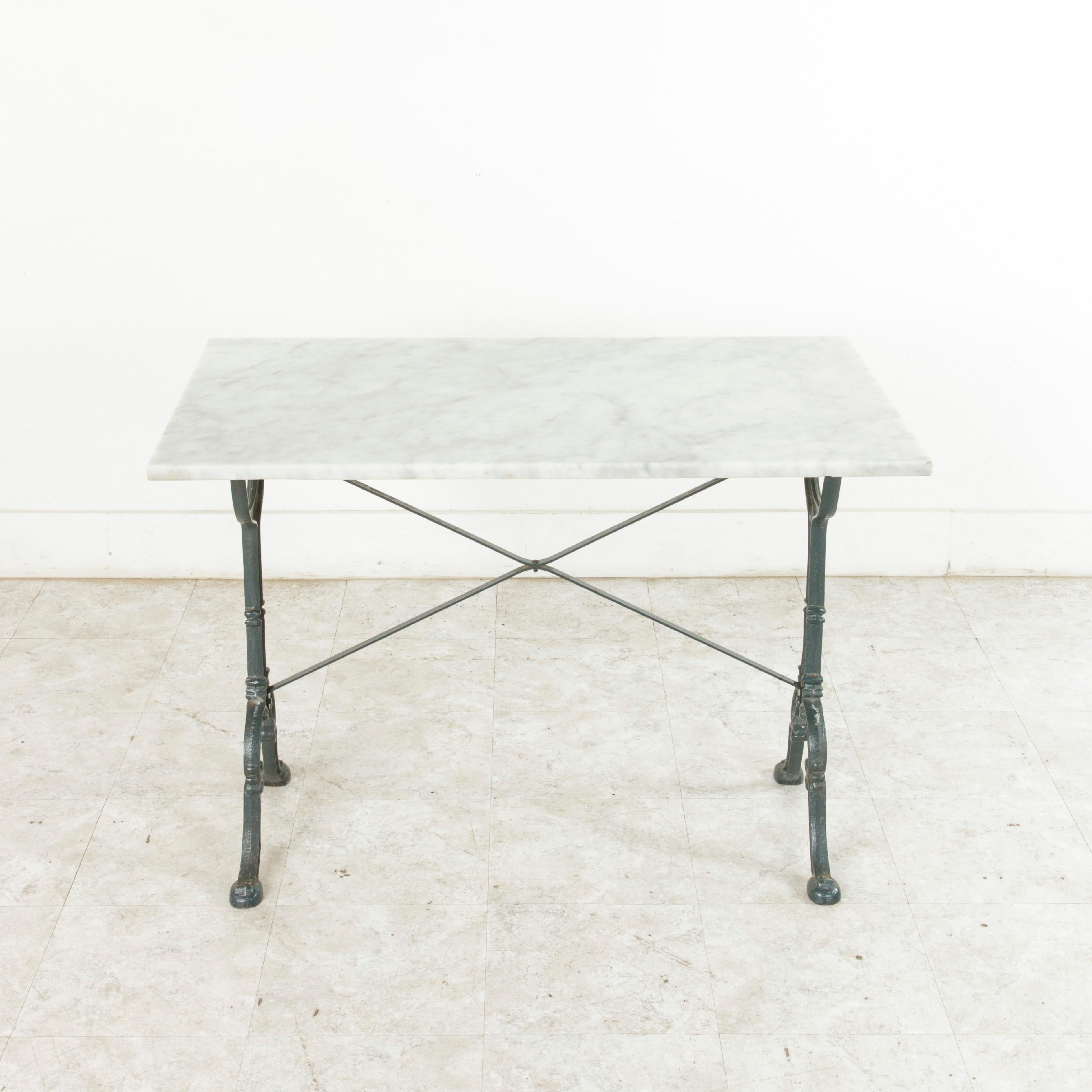 This early 20th century cast iron bistro table features its original solid marble top. A riveted stretcher provides additional stability. The base is marked by the maker Godin, a French company also well-known for its cast iron stoves. Ideal as a