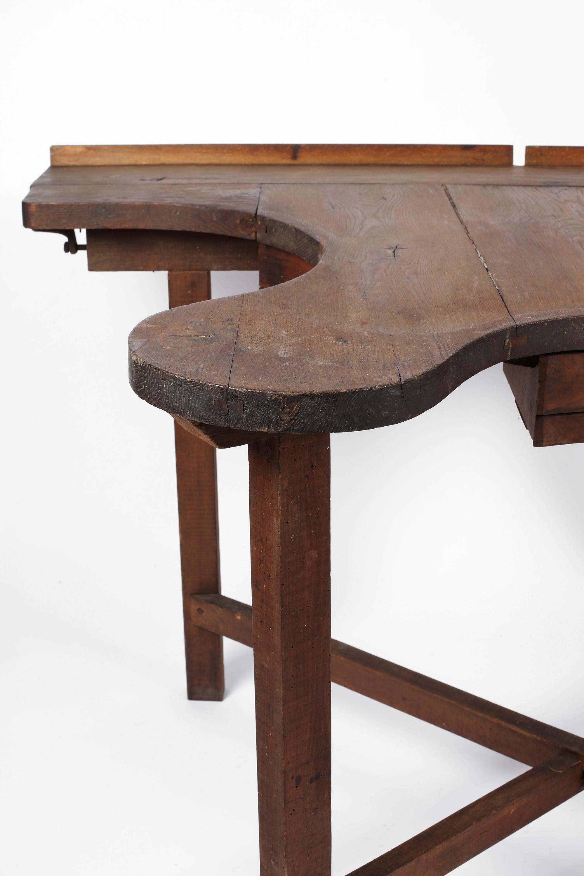 Característica mesa de trabajo de joyero de principios del siglo XX, de roble patinado, que conserva sus cajones, ganchos para herramientas y pinzas originales. Con el sello distintivo de su pasado utilitario, es adecuada como mesa central, para