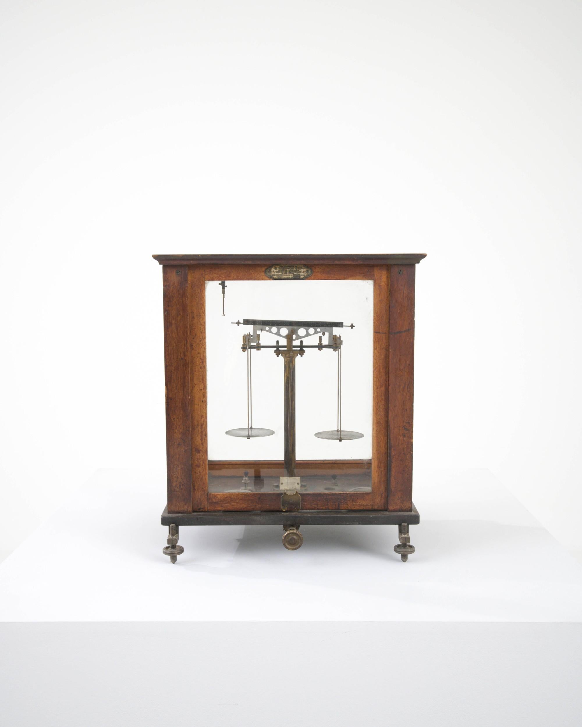 Housed in a wooden and glass vitrine, this small scale was once used for precision measurements. Made at the turn of the 19th Century in France, this mechanical wonder was crafted with an eye for aesthetics, the richly polished wood and meticulously