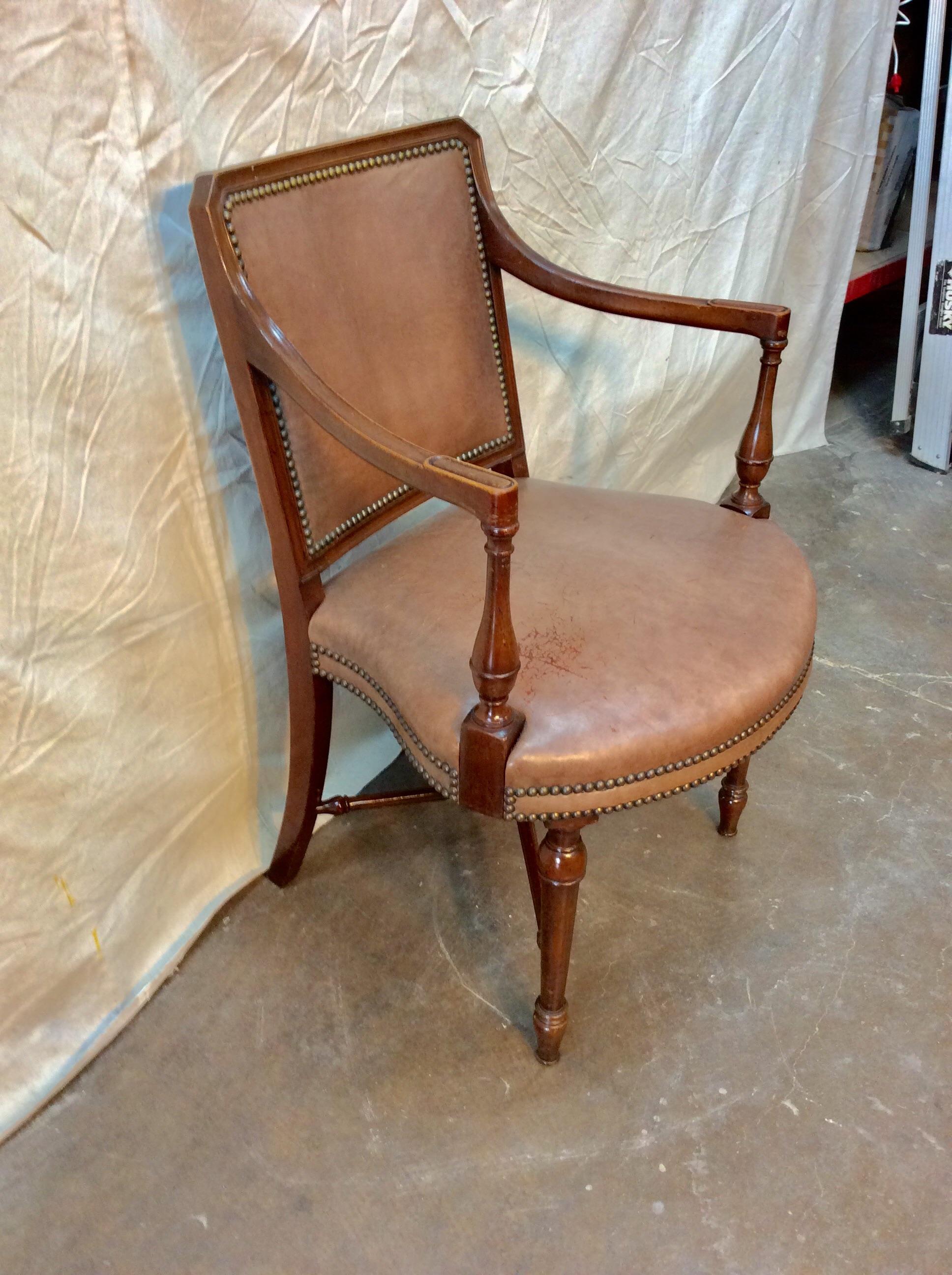 Presented as found, this Early 20th century French Armchair features a walnut wood frame and soft tan leather upholstery. Brass nailheads accent the rounded seat as well as the front and back of the chair. Resting on four legs with a double crossbar