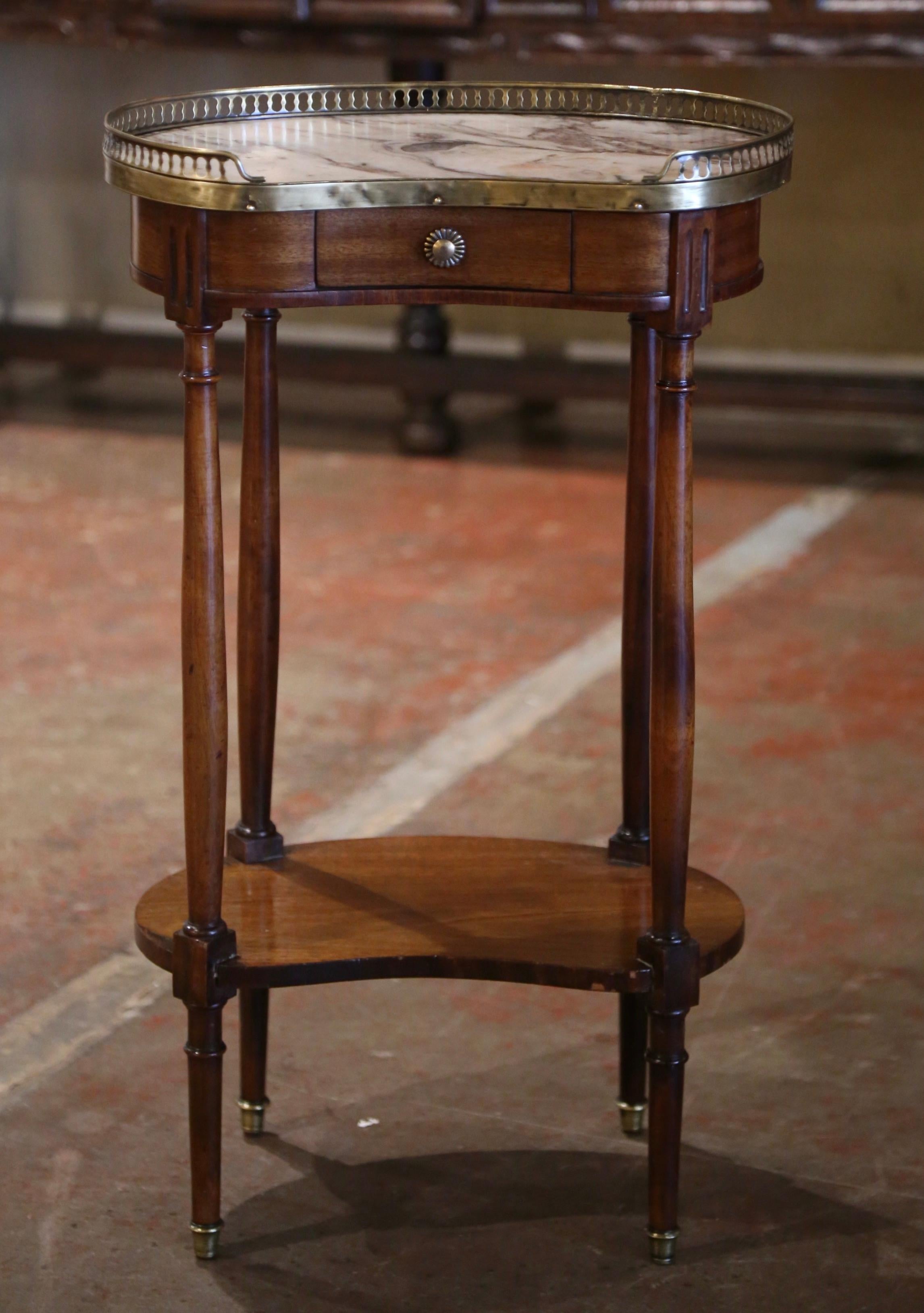 Cette élégante table d'appoint en forme de rein a été fabriquée en France vers 1920. Construite en bois d'acajou, la petite table repose sur de minces pieds tournés se terminant par des pieds effilés, décorés d'une étagère inférieure. La surface