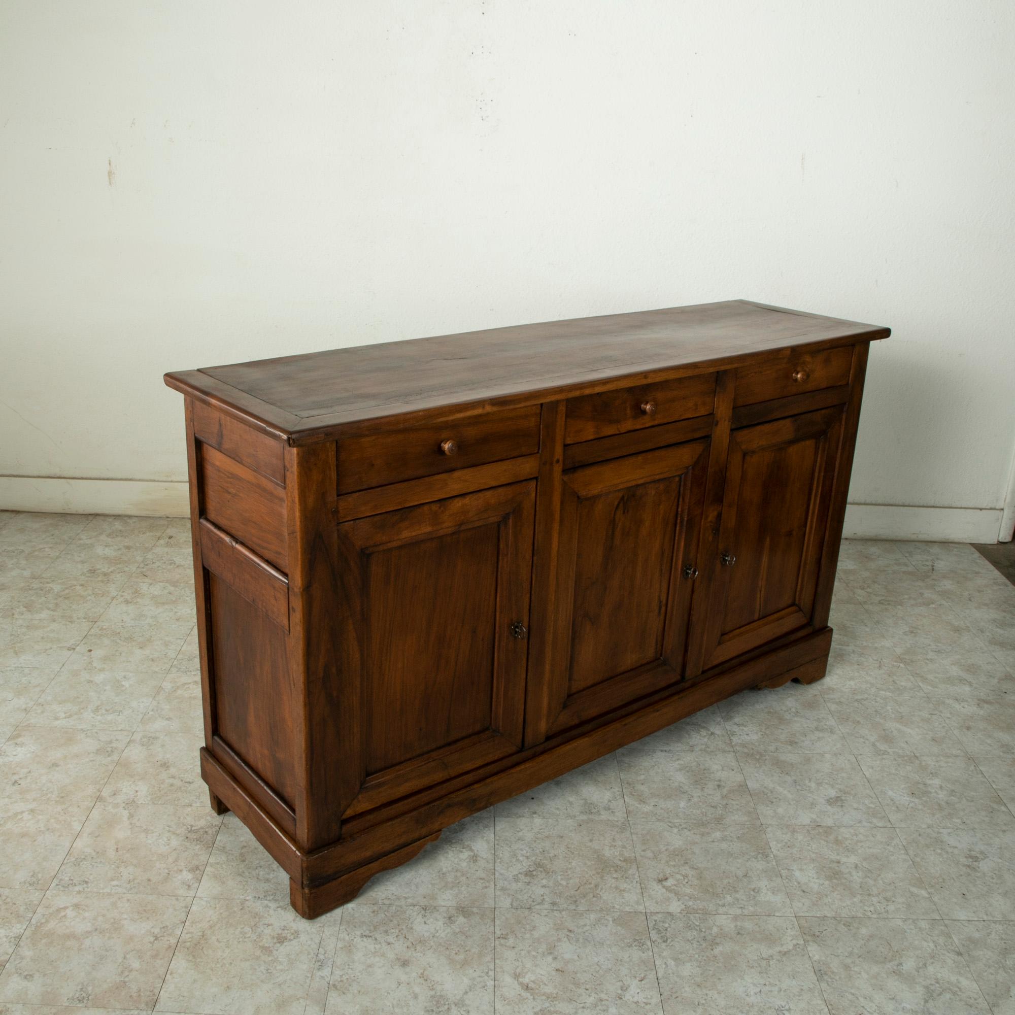 This French Louis Philippe style enfilade or sideboard from the early 20th century is constructed of solid walnut with hand pegged joinery. This server features three doors that open to reveal an interior with a single shelf. Behind each door is a