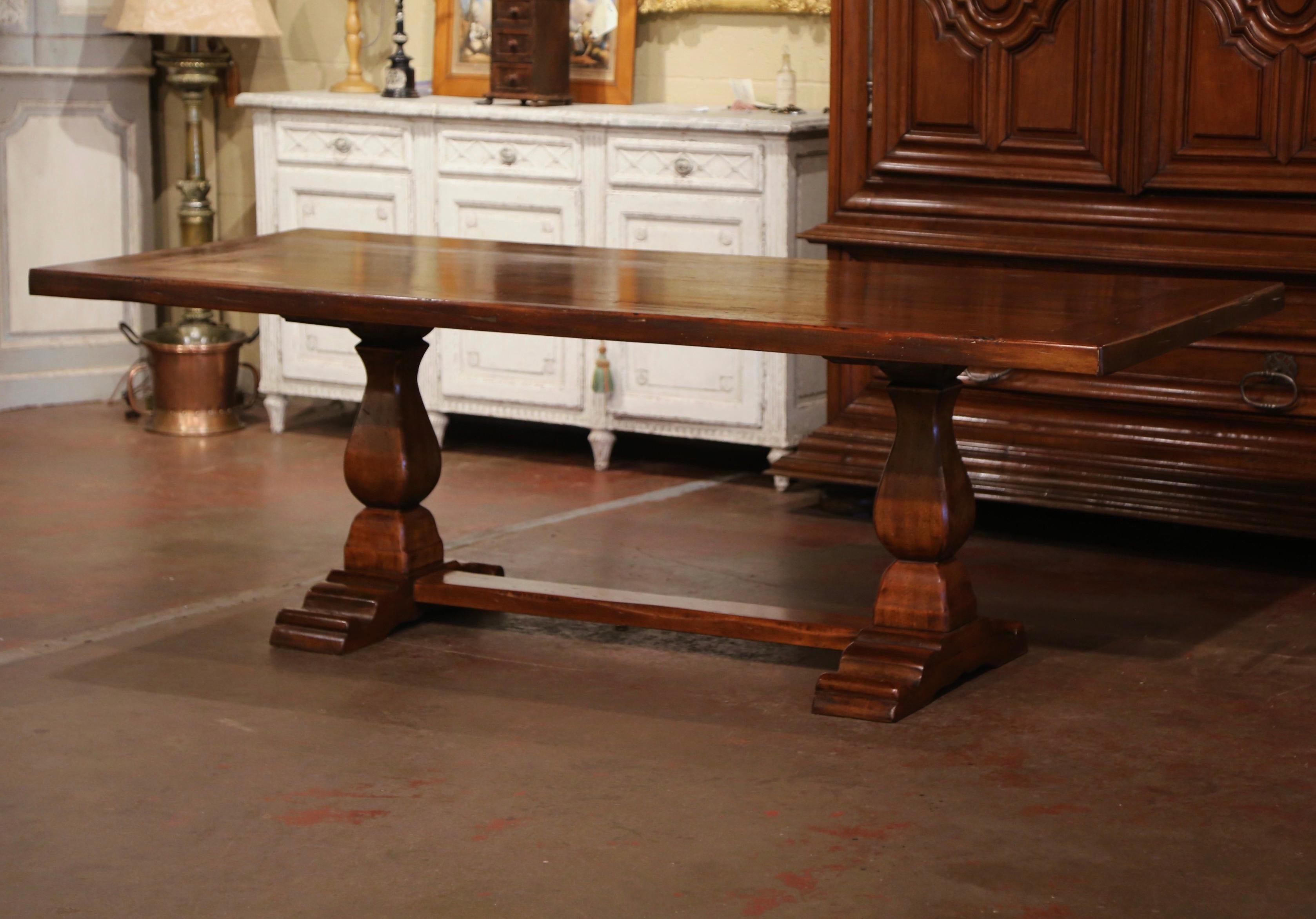 This elegant antique refectory dining table was crafted in France, circa 1920. Standing on two carved baluster form legs ending with shoe feet and joined with a bottom stretcher, the Baroque monastery table is dressed with a solid 2