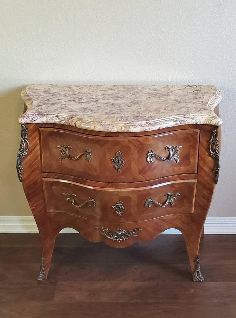 A gorgeous, exquisitely crafted antique Louis XV style mahogany inlaid commode ornamented with chiseled and gilded bronze throughout. Hand crafted in France during the early 20th century having serpentine shaped marble top with moulded edge, above
