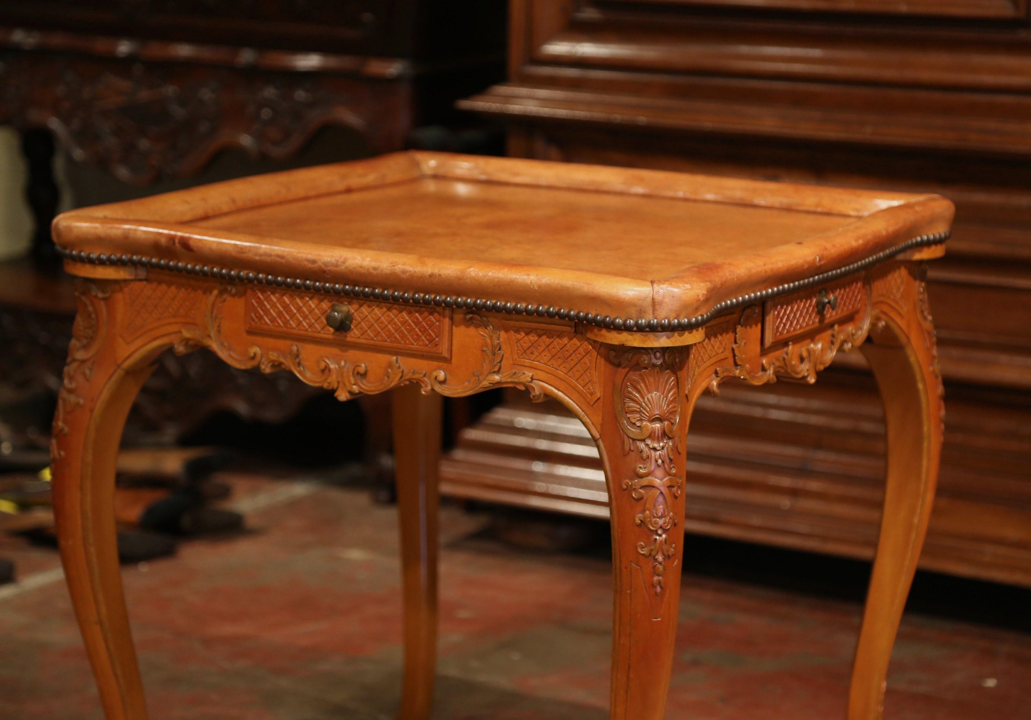 Crafted in France circa 1920 and square in shape, the fruit wood table stands on cabriole legs ending with escargot feet at the base. The table with a scalloped apron is decorated with carved leaf motifs at the shoulders. The small, charming table