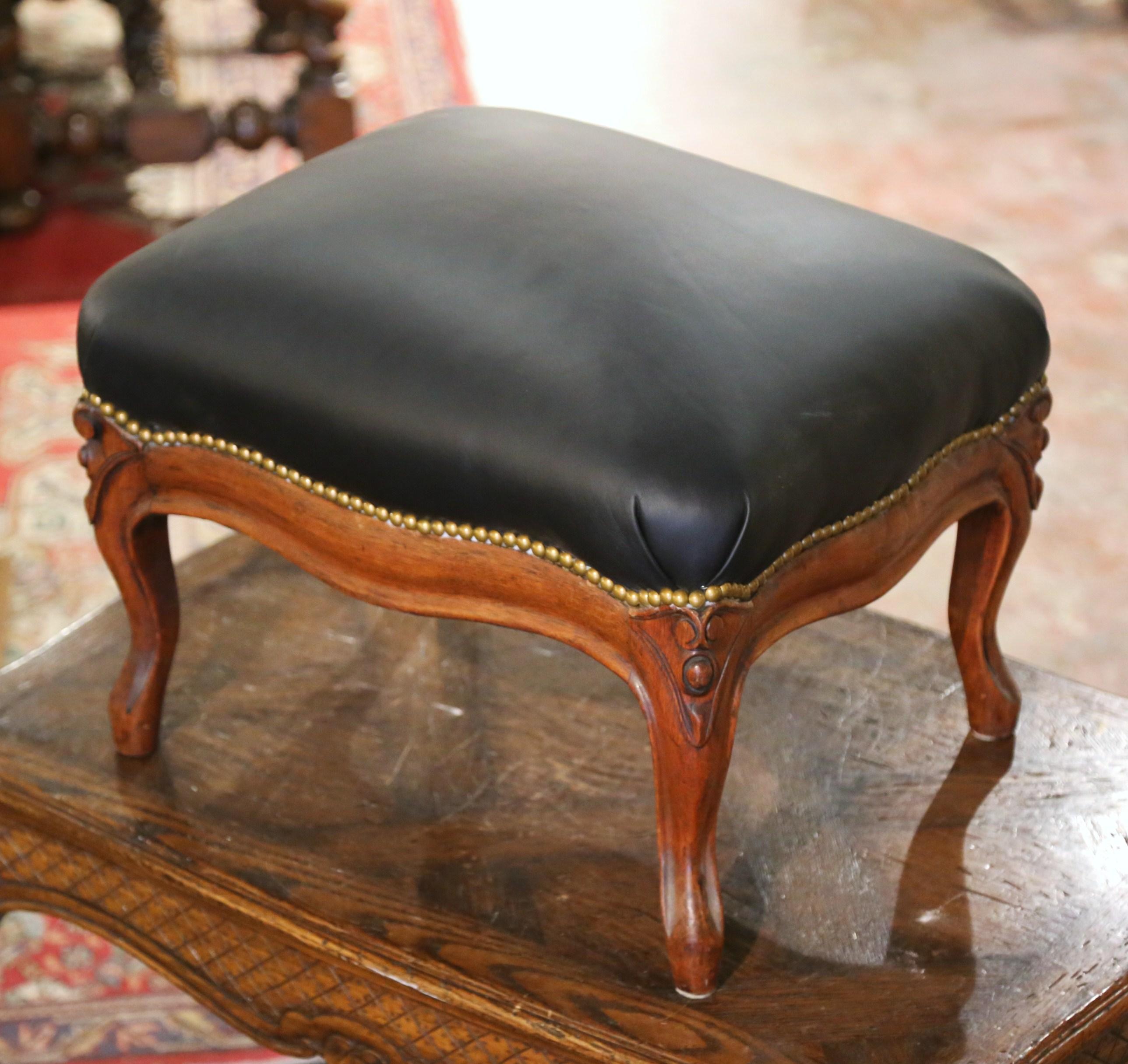 This elegant, antique Louis XV stool was crafted in France, circa 1920. The large rectangular footstool sits on four cabriole legs decorated with scrolled motifs at the shoulders over a scalloped apron. The seat is upholstered with a black leather,