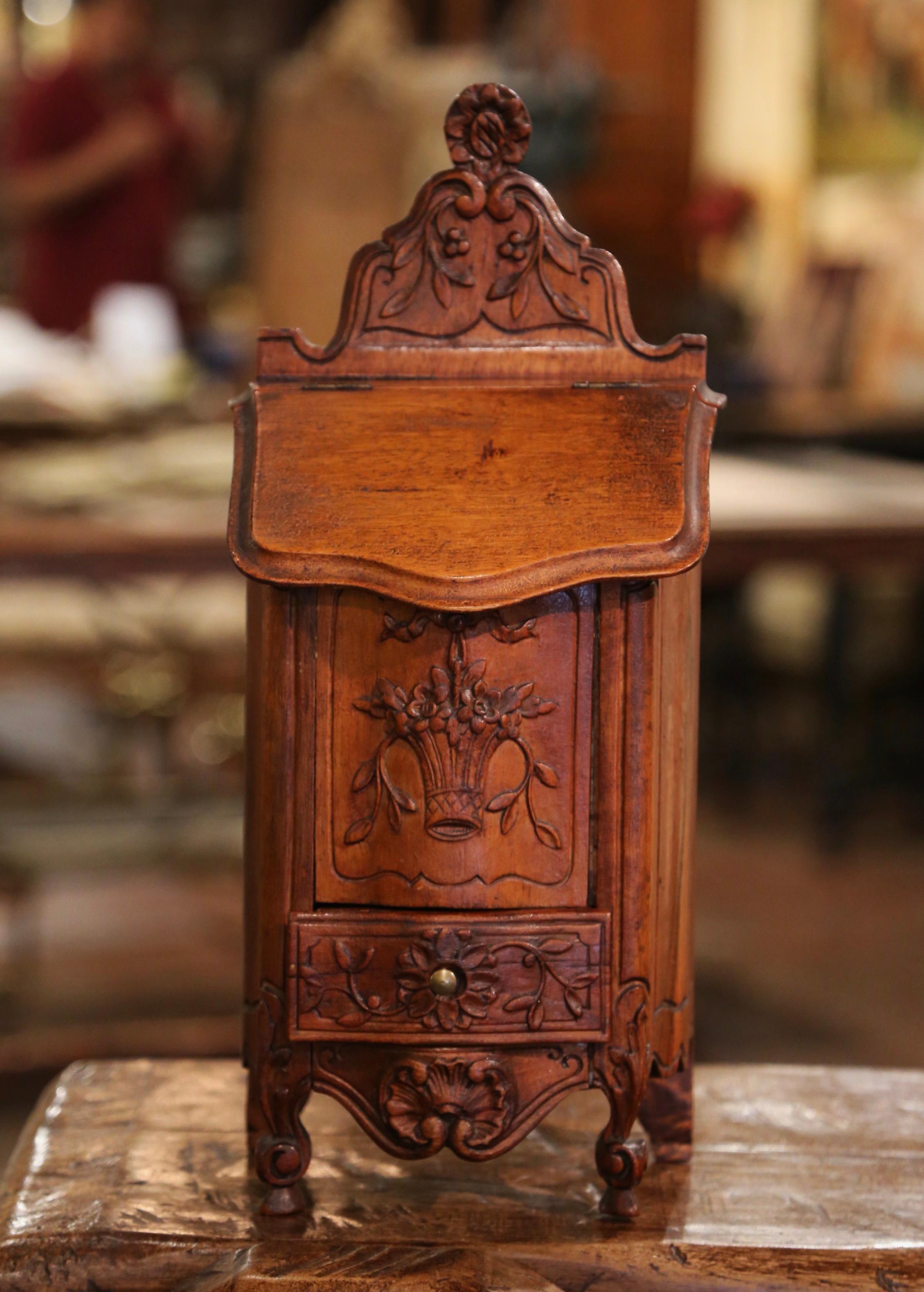 This elegant, antique fruitwood salt box was crafted in southern, France, circa 1920. The ornate, decorative, walnut box sits on delicate escargot feet over a scalloped apron decorated with a shell motif; it features beautiful carvings throughout