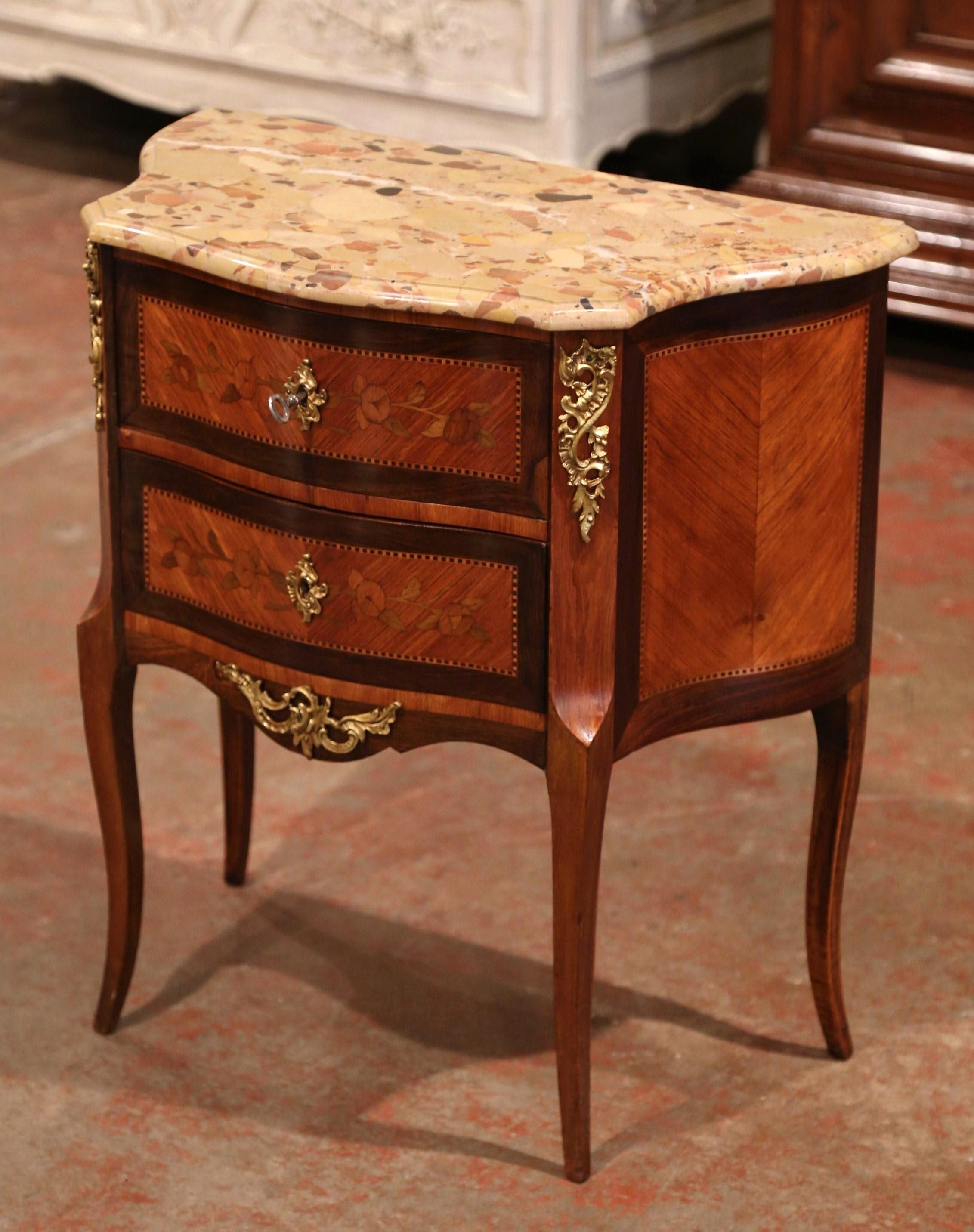 Crafted in France, circa 1920, the two-tone fruitwood cabinet sits on cabriole legs; it features two bombe drawers across the front decorated with inlay and veneer floral embellishments. The commode is further dressed with bronze mounts over the