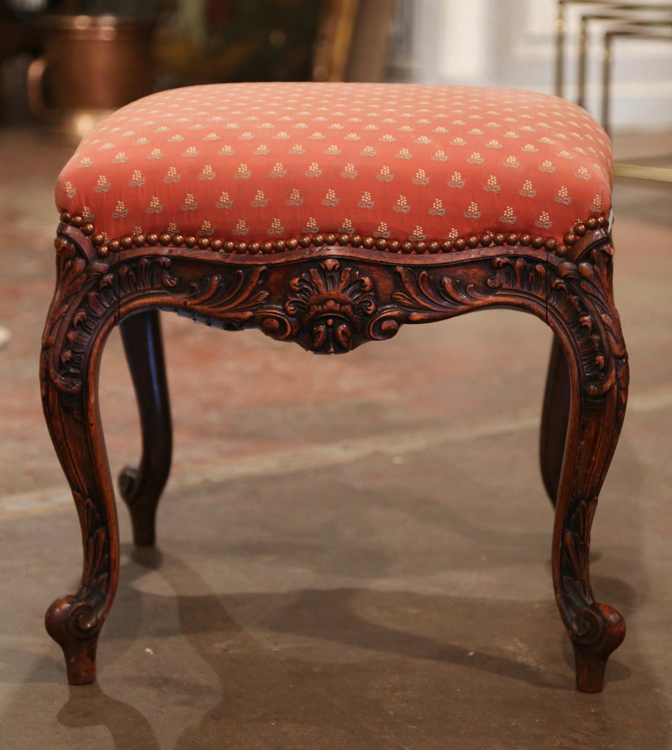 Use this heavily carved stool as extra seating in a den or living room! Crafted in southern France circa 1920 and square in shape, the stool stands on elegant cabriole legs decorated with acanthus leaf motifs at the shoulders and ending with
