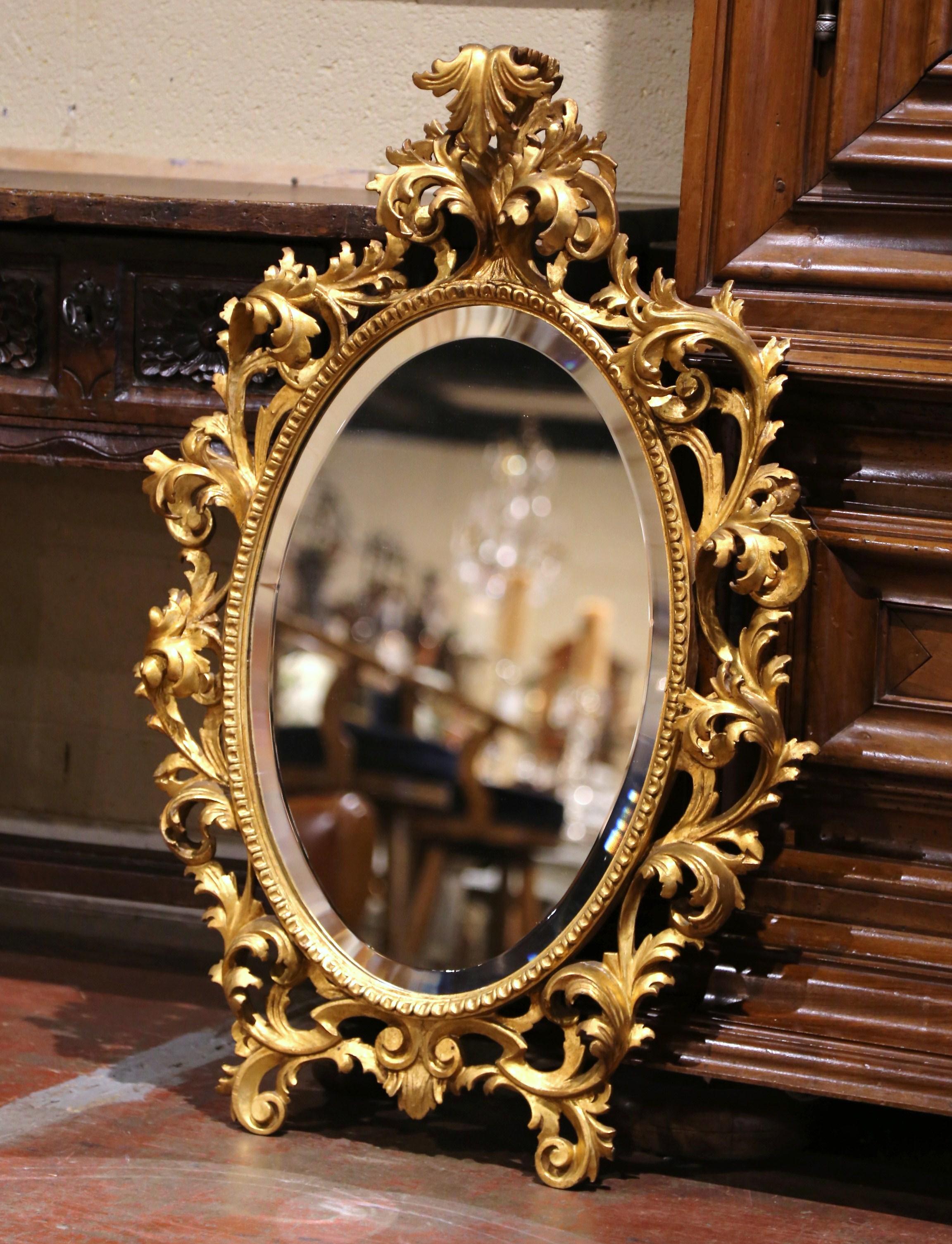 Decora un tocador o una entrada con este elegante espejo dorado antiguo. Fabricado en Francia hacia 1920, el ornamentado marco perforado presenta una cartela con decoración de hojas en el frontón, flanqueada por curvas fluidas, motivos florales y