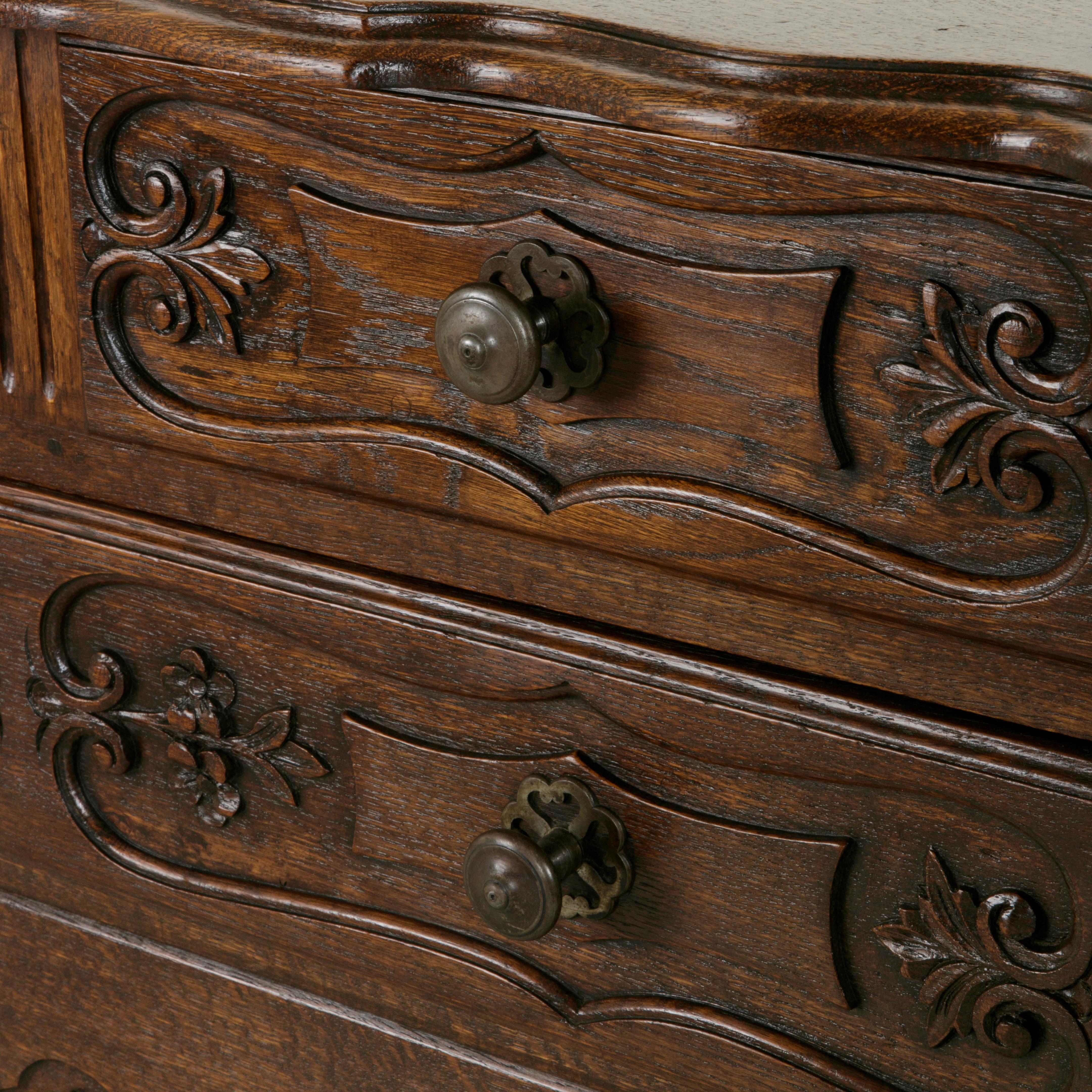 This early 20th century French Louis XV style oak commode sauteuse or chest features hand carved details of leaves, flowers and scrolling and is finished with a beveled oak top made from a single plank of wood. A commode sauteuse or 
